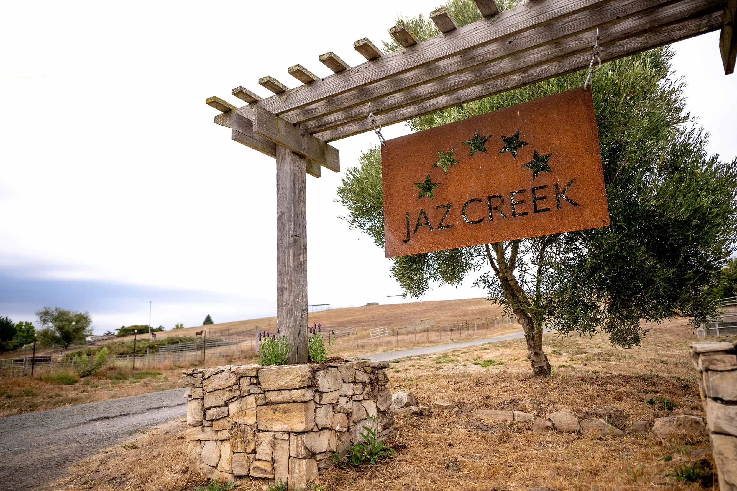 A copper metal sign with five stars and the name Jaz Creek hanging from a wooden pergola
