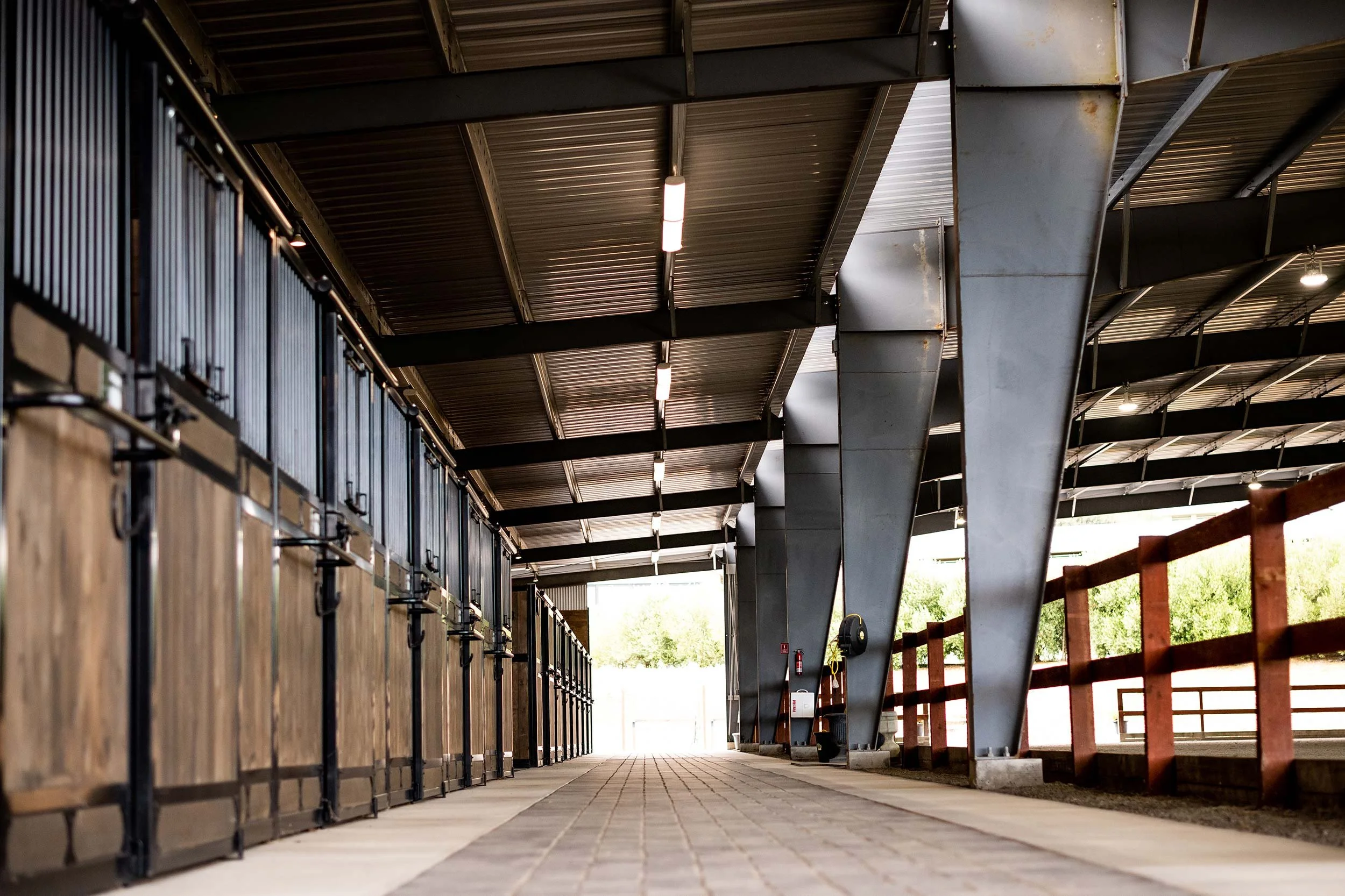 Barn aisle with large stalls on the left and indoor arena fence to the right