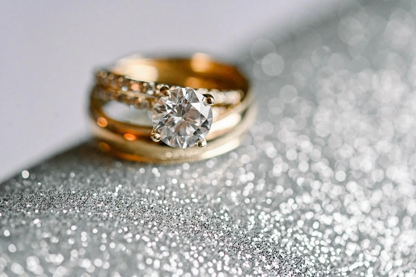 Close-up of a gold ring with a large diamond on a glittery surface.