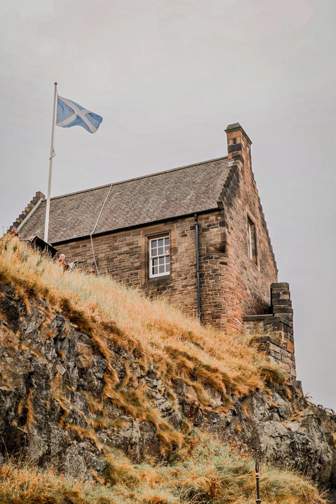 stone wall with grass and stone building behind it