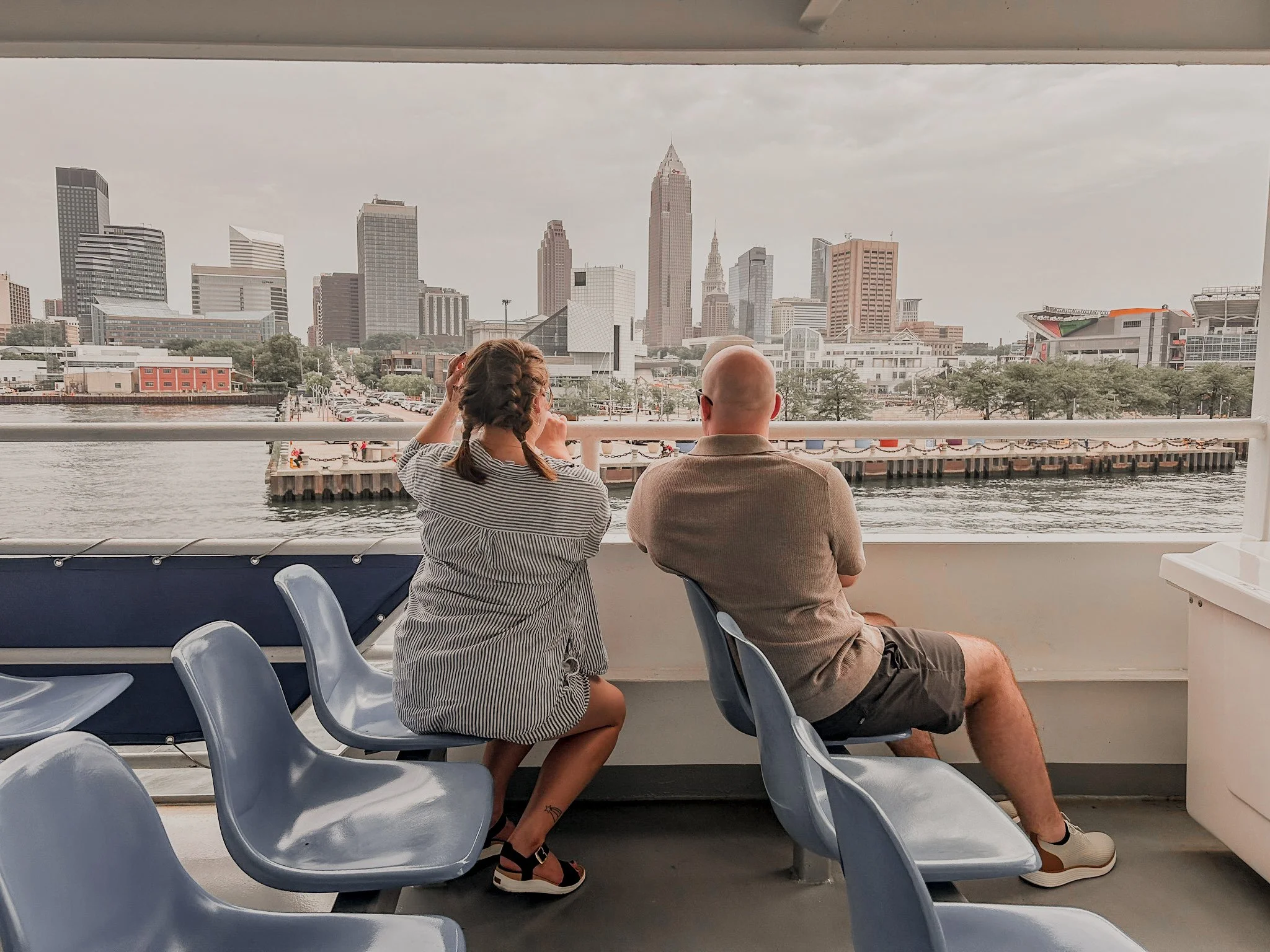 A woman with french braids and a man in a tan shirt on a boat over looking a city skyline