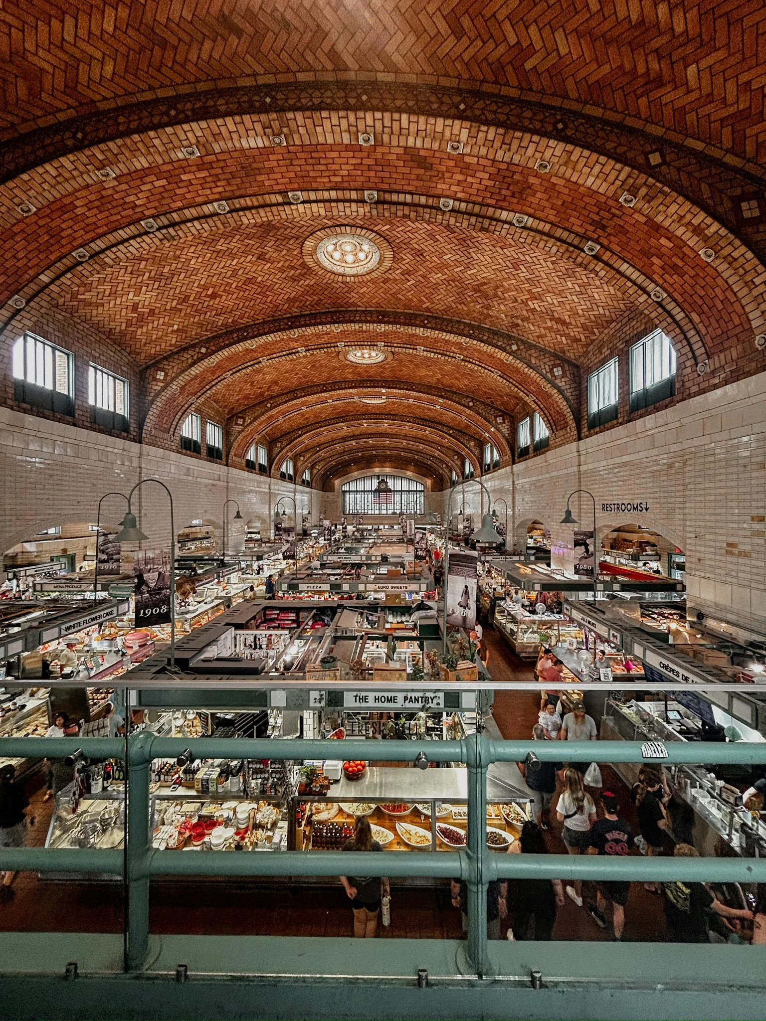 A photo of a food hall. The ceiling is curved and made of chevron style brick. The floor is covered with food stalls from different vendors