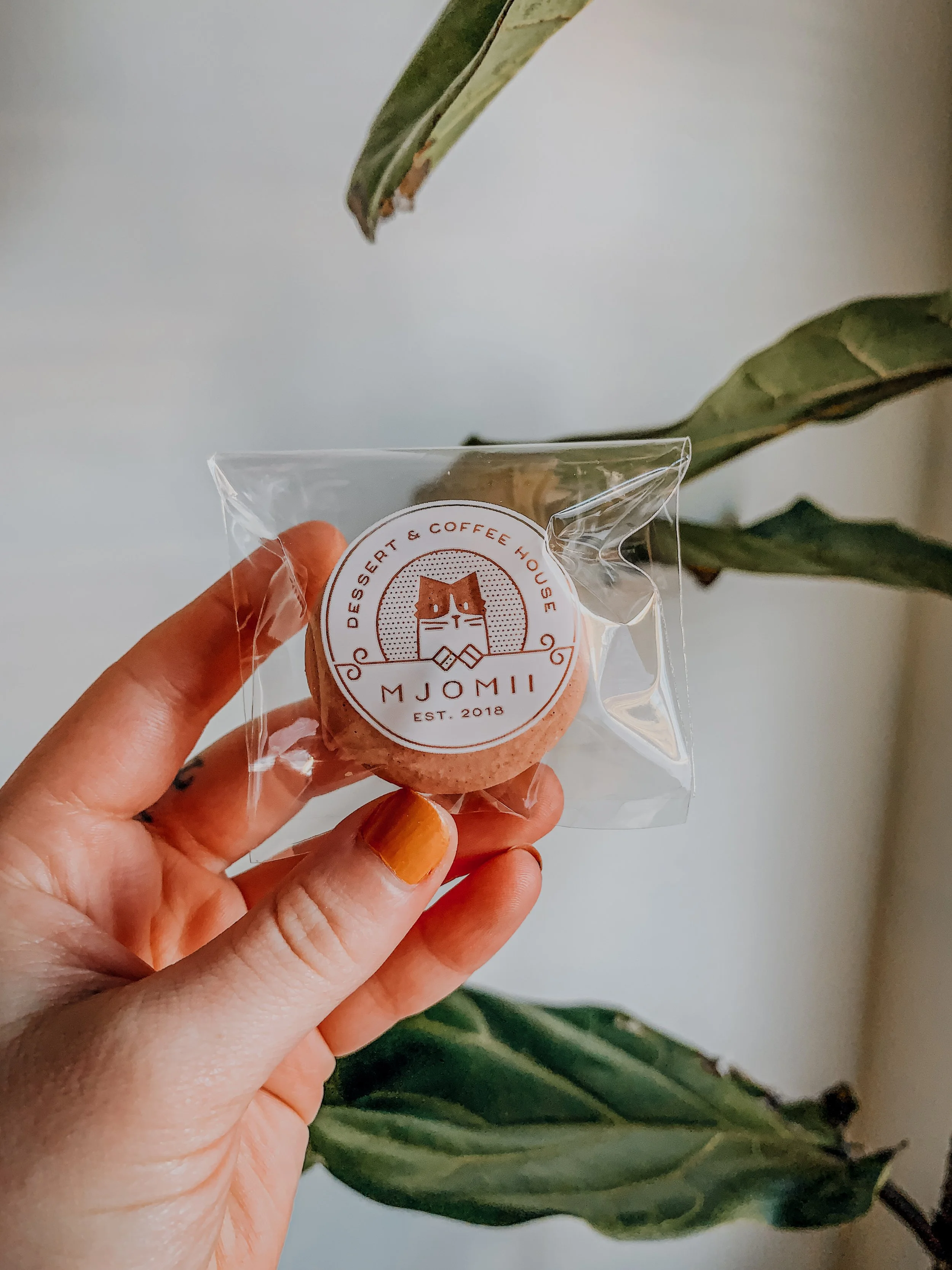 A macaron wrapped in plastic with a sticker on front being held by a hand