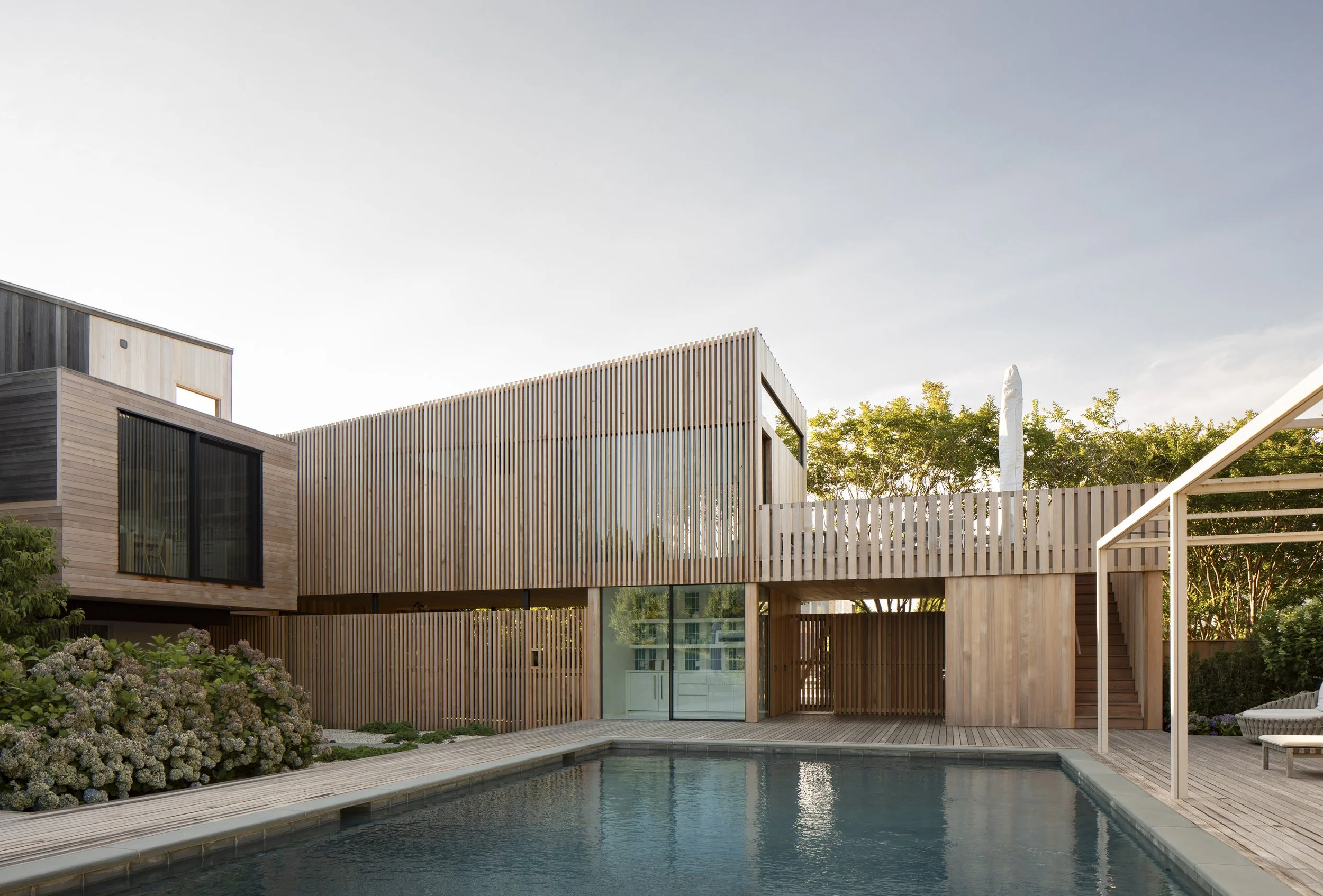Modern house with wooden exterior, large windows, and a backyard pool with surrounding deck and greenery.