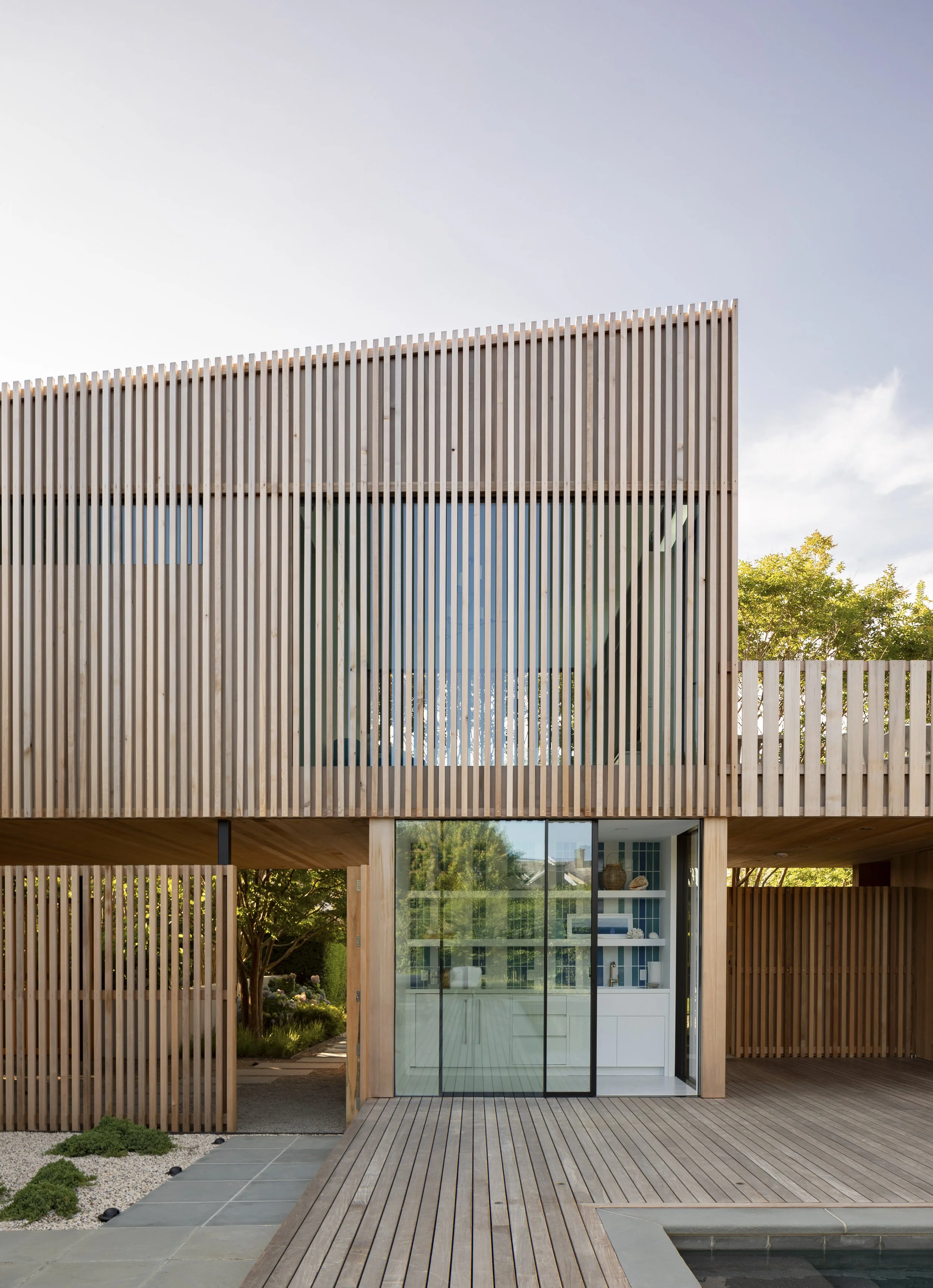 Modern two-story house with wooden slat exterior, large glass doors, and an outdoor wooden deck.