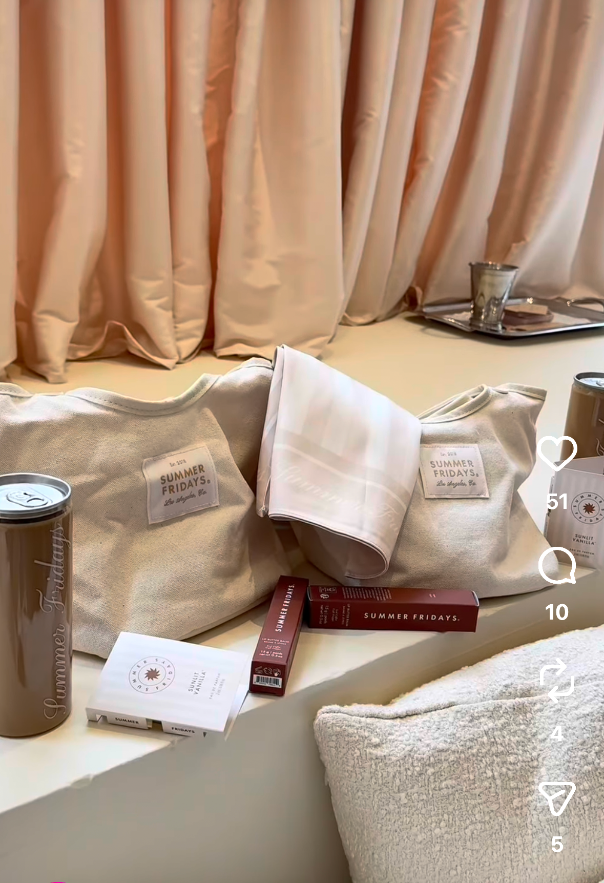 Summer Fridays “Sun Room” pop-up display featuring neutral-toned branded tote bags, skincare and beauty products, a reusable tumbler, and boxed items arranged on a cream ledge in front of soft beige curtains.