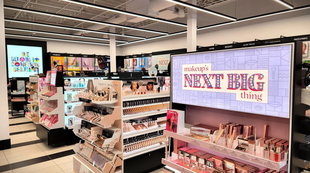 Sephora retail display featuring the “Next Big Thing” makeup wall, with shelves of foundation, lip products, and beauty items arranged in rows beneath a large digital sign reading “makeup’s NEXT BIG thing,” inside a brightly lit cosmetics store