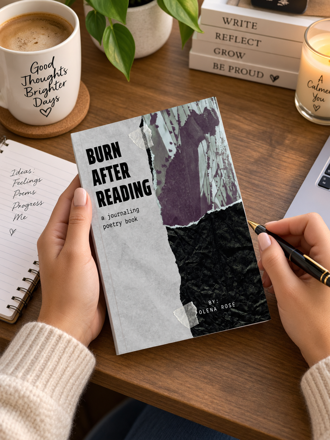 A person holding a journaling poetry book titled 'Burn After Reading' by Olena Rose, on a wooden desk with a coffee mug, a notebook with handwritten ideas, a potted plant, a lit candle, and a stack of books with motivational titles.