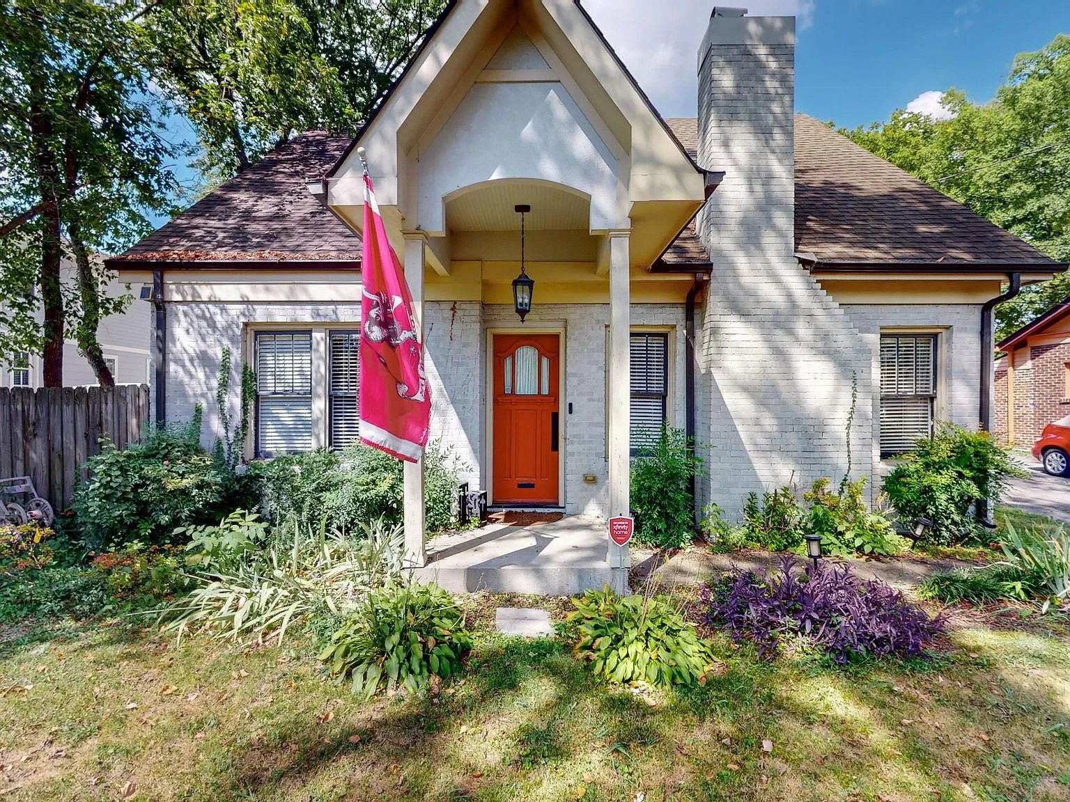 Cottage-style Nashville home with brick exterior, orange front door, and mature garden landscaping..webp