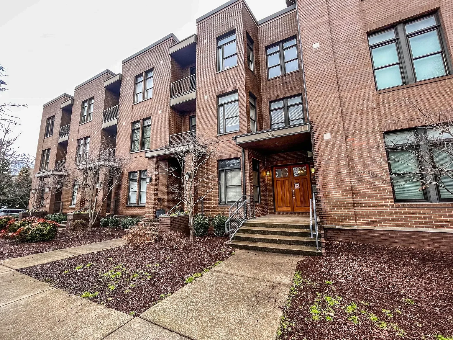 Front entrance of a brick mid-rise Nashville condo building with balconies and landscaped walkways..webp
