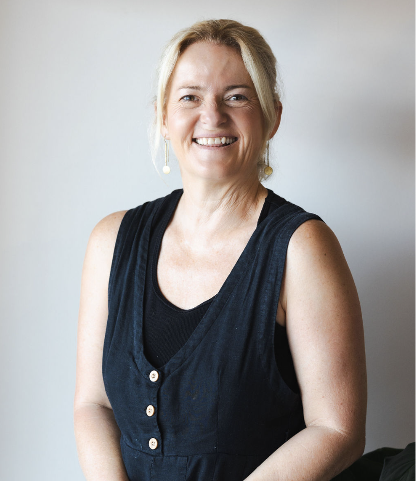 A woman with blonde hair wearing a sleeveless black top and earrings, smiling at the camera against a plain light background.