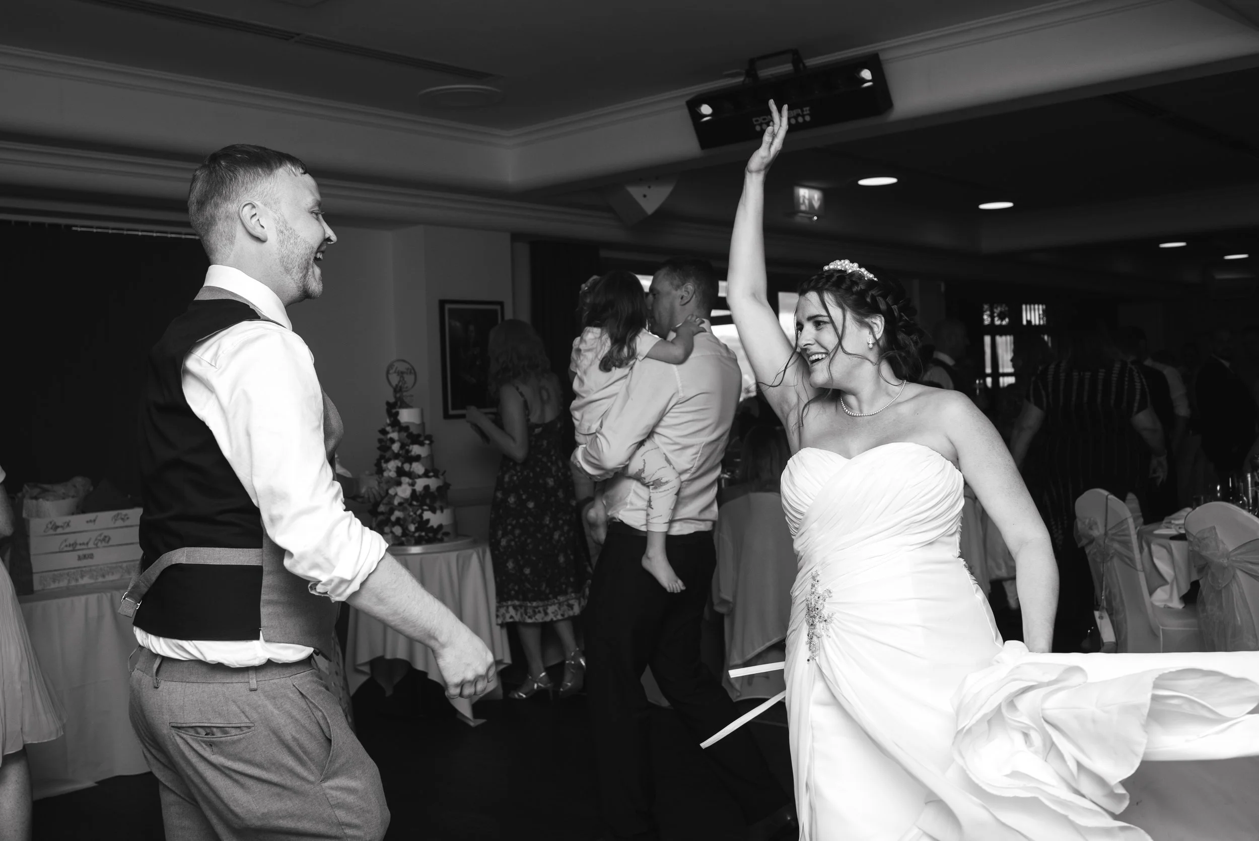 Wedding reception scene with a bride and groom dancing and smiling, surrounded by guests in the background.