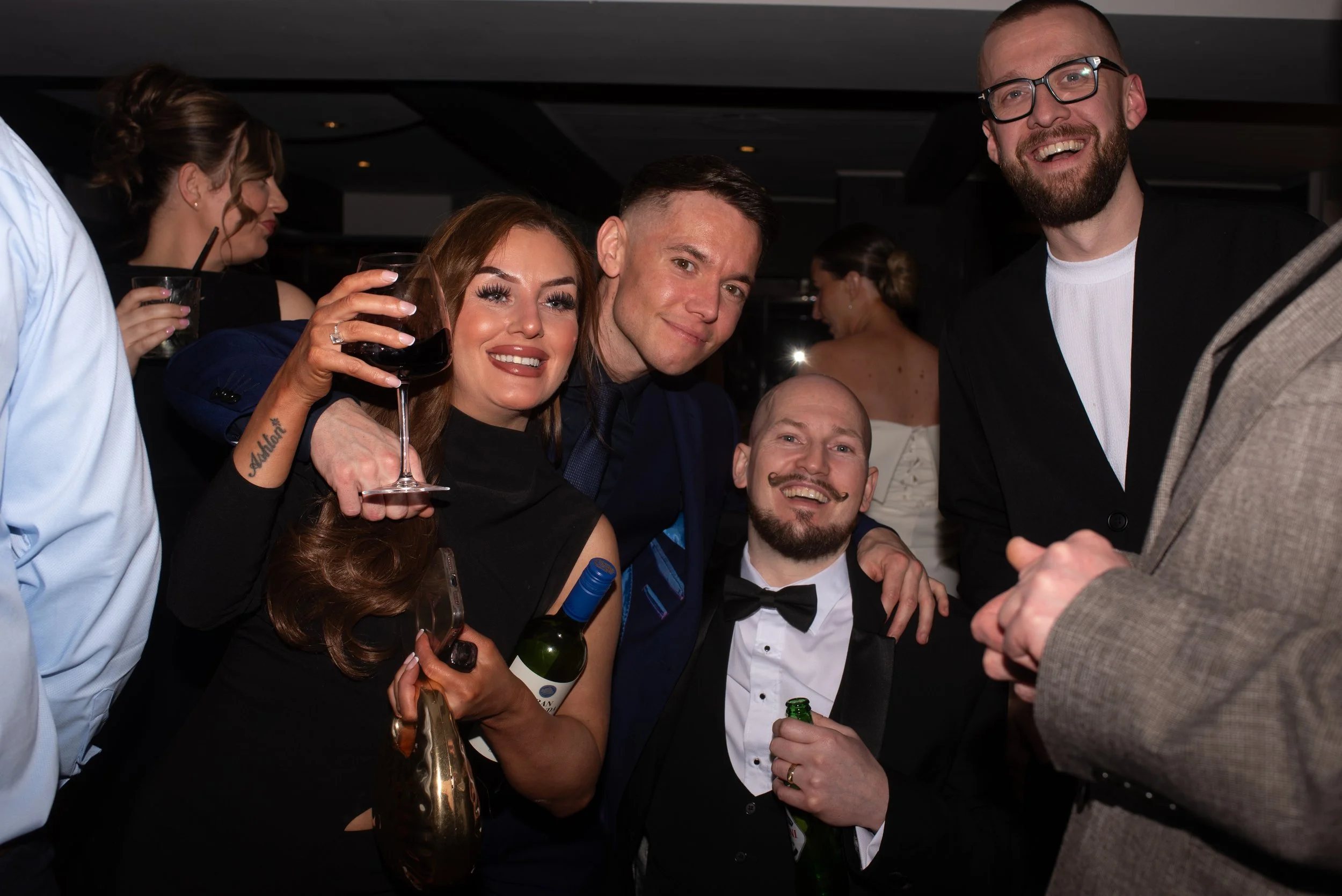 Group of friends dressed in formal attire enjoying a celebration at a party or wedding reception, smiling and holding drinks.