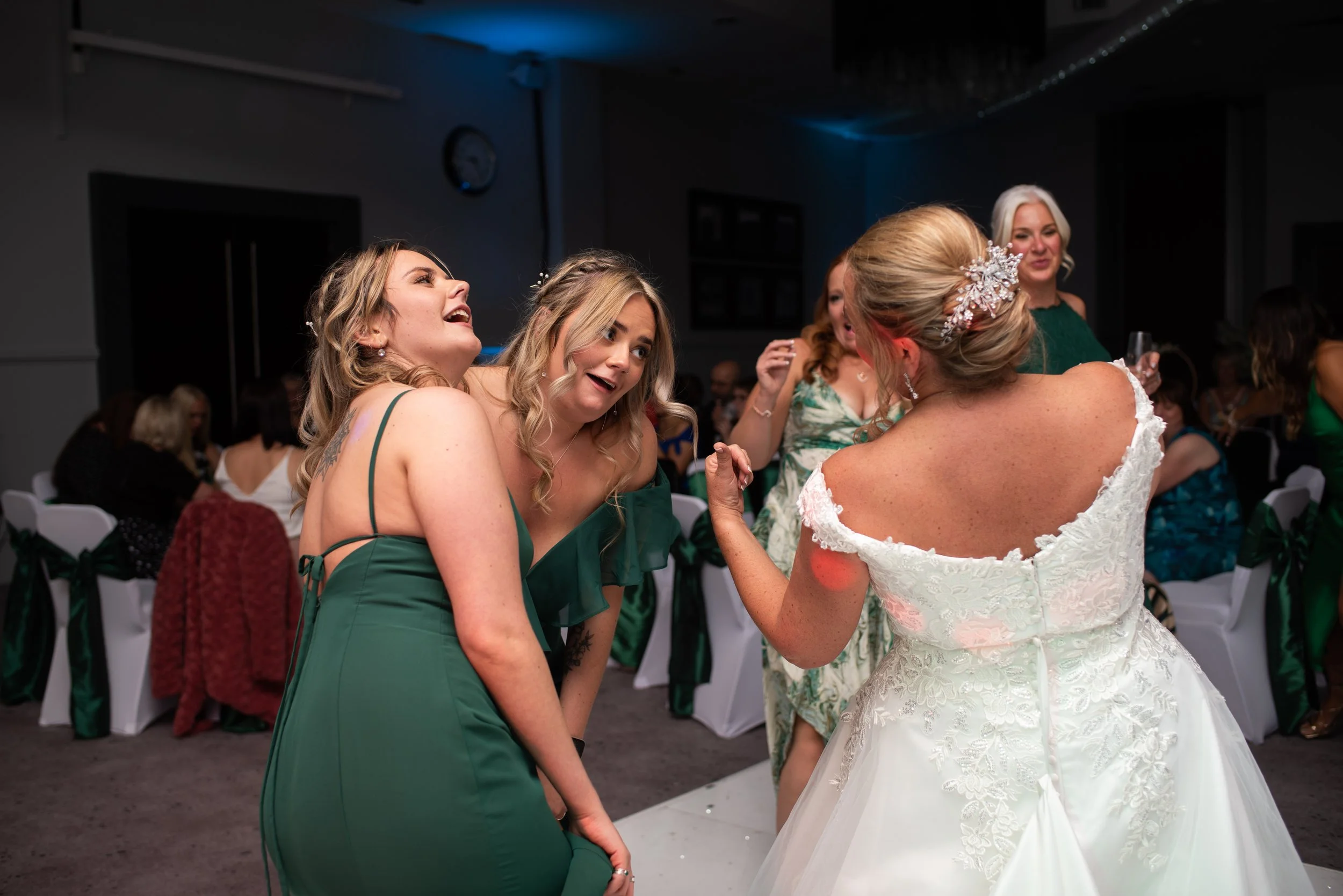 Women dancing and celebrating at a wedding reception, including a bride in a white dress with an ornate hair accessory, and her friends in green dresses.