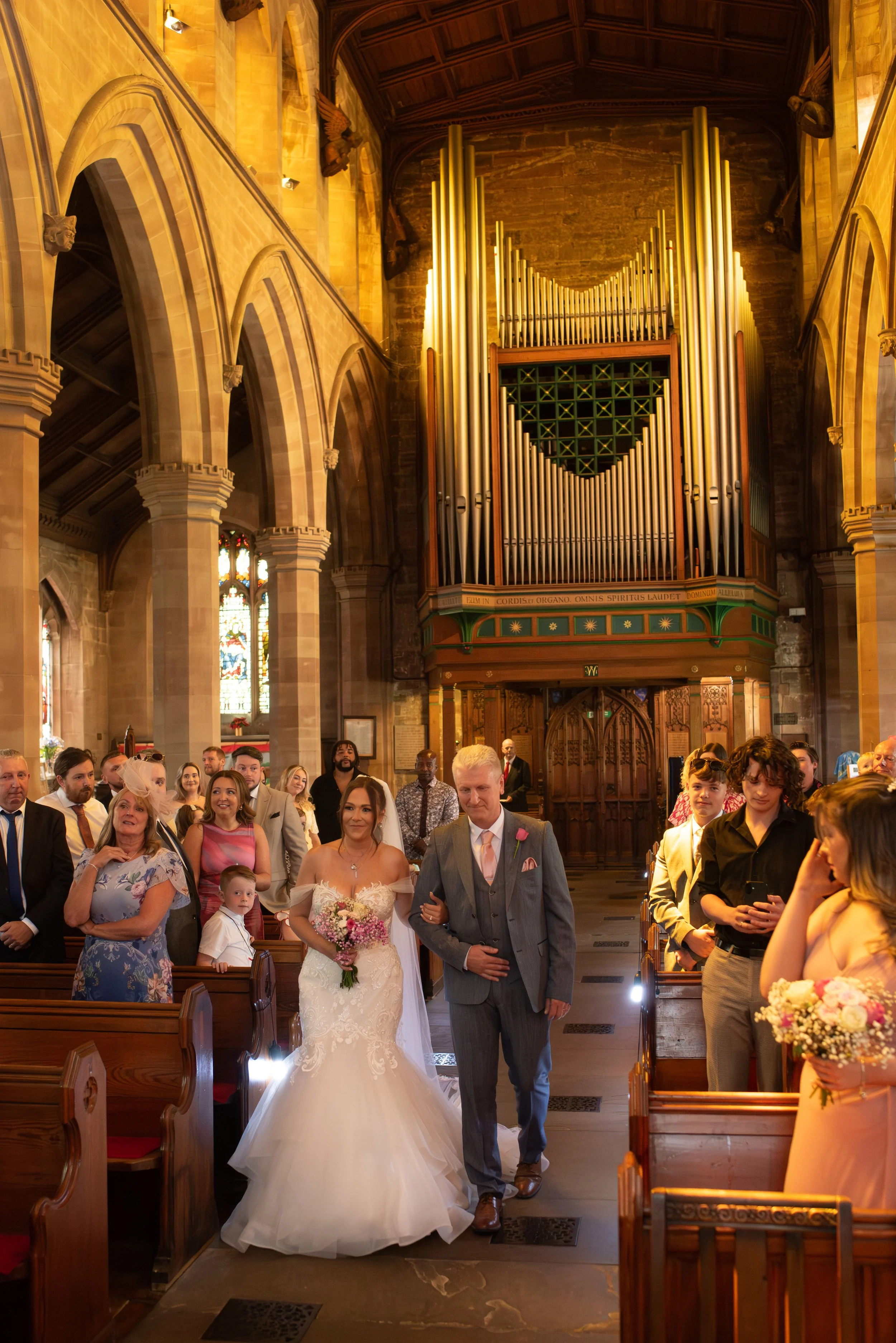 Bride walking down the aisle with her father in a church during her wedding ceremony, surrounded by guests.