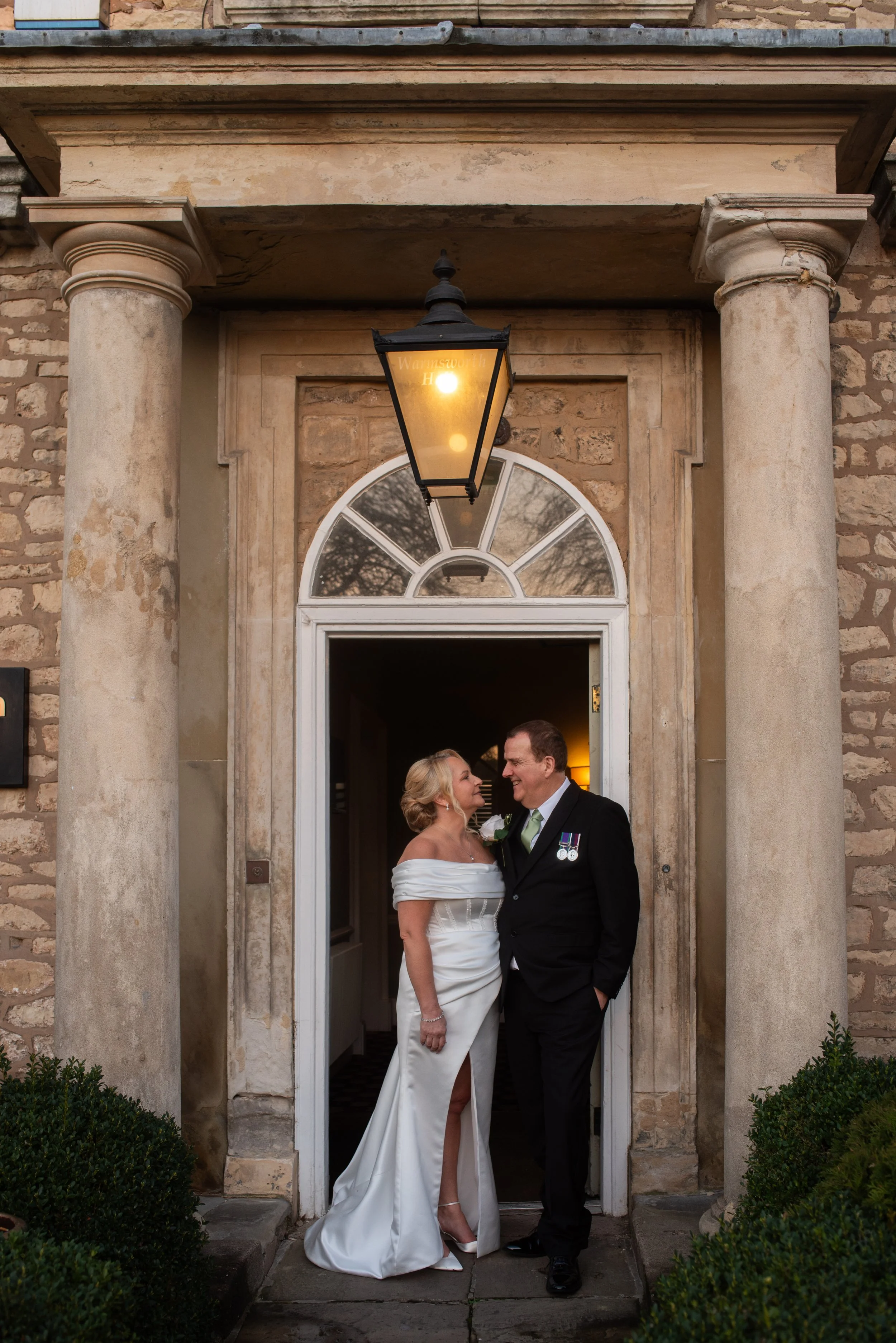 Bride and groom standing at the doorway of a historic building, sharing a happy moment on their wedding day.