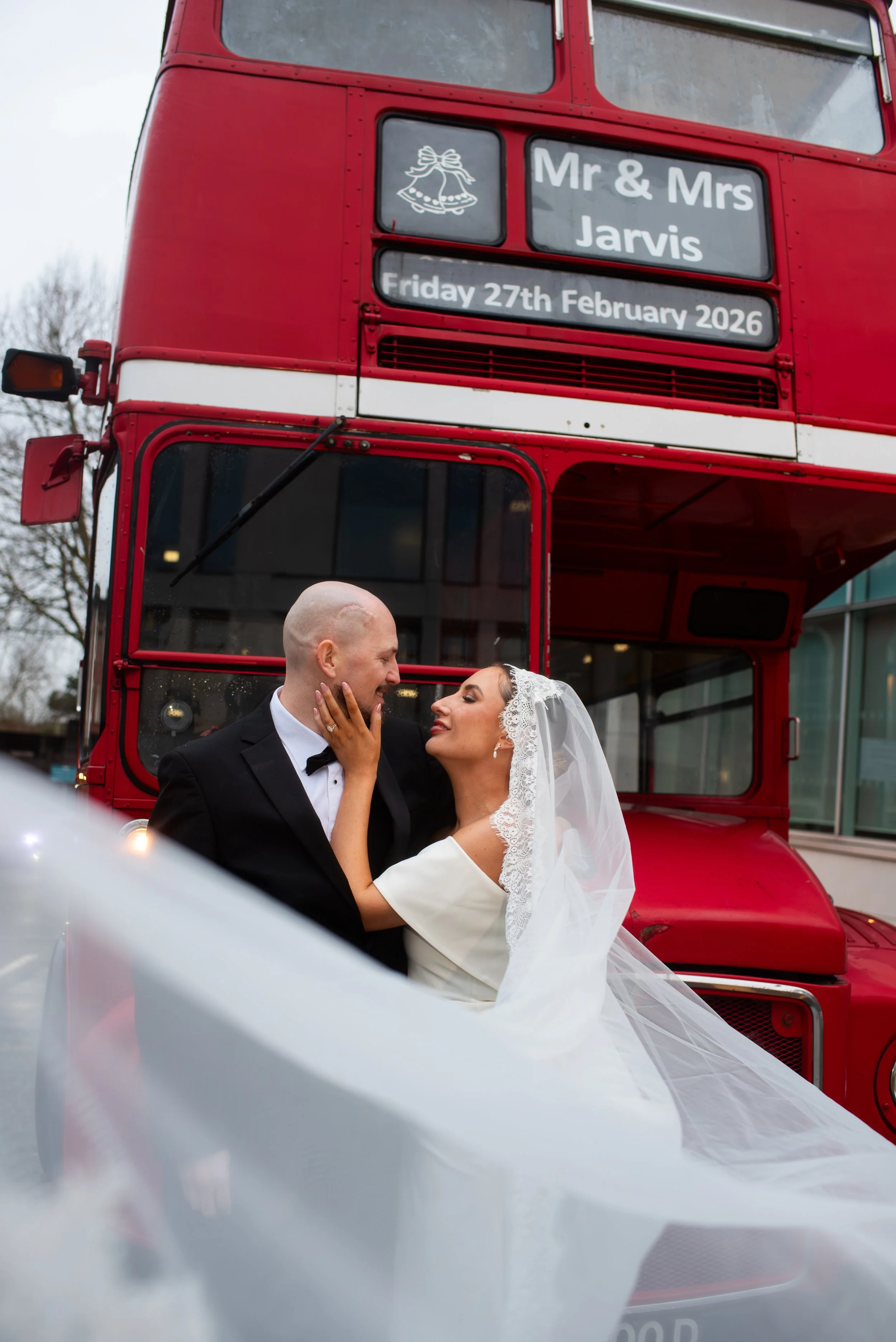 Bride and groom kissing outdoors with a scenic landscape and cloudy sky in the background.