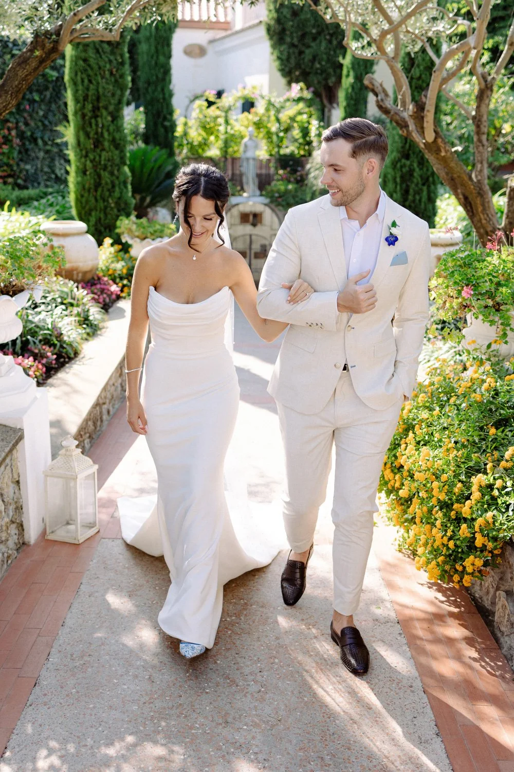 A bride and groom walking arm in arm in a garden, smiling and enjoying each other's company.