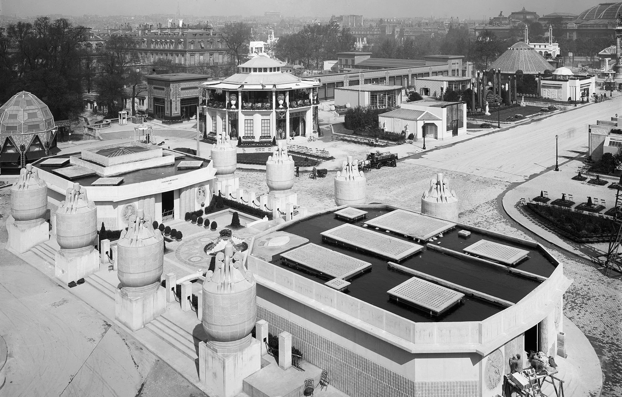 High-angle historical view of the 1925 Paris International Exposition grounds, showing various pavilions, water features, and surrounding architecture.