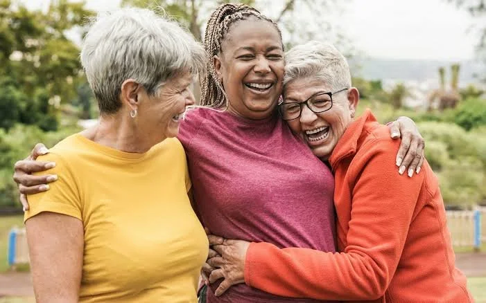 Three adults laughing and hugging outdoors.