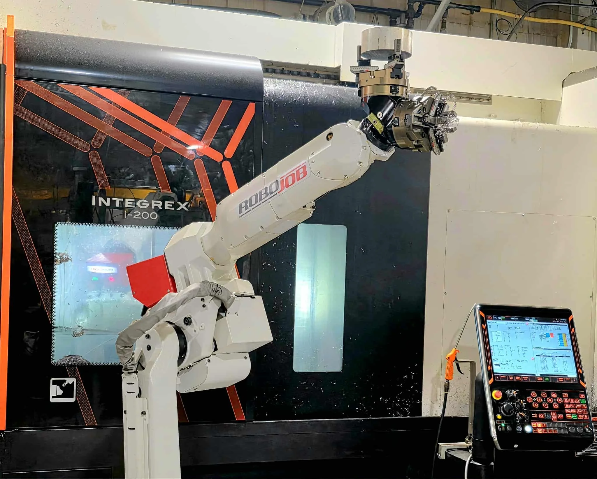 An industrial robotic arm with a white and red Robojob end effector is operating inside a CNC machine labeled 'INTREX' and 'i-200'. The robot is engaged in machining or manufacturing, with a control panel on the right for programming and operation.