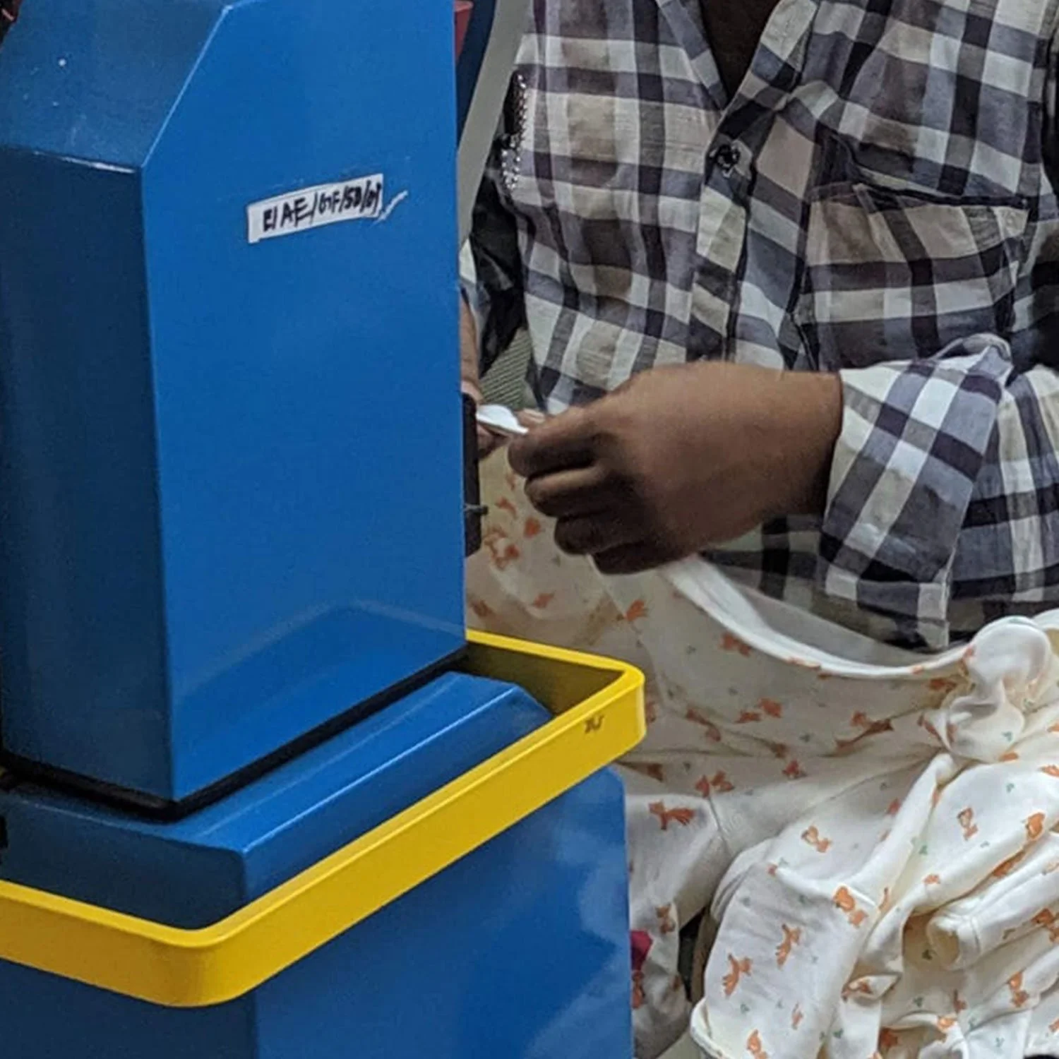 Baby fox sleepsuit having poppers applied in a factory by a person wearing navy checked shirt