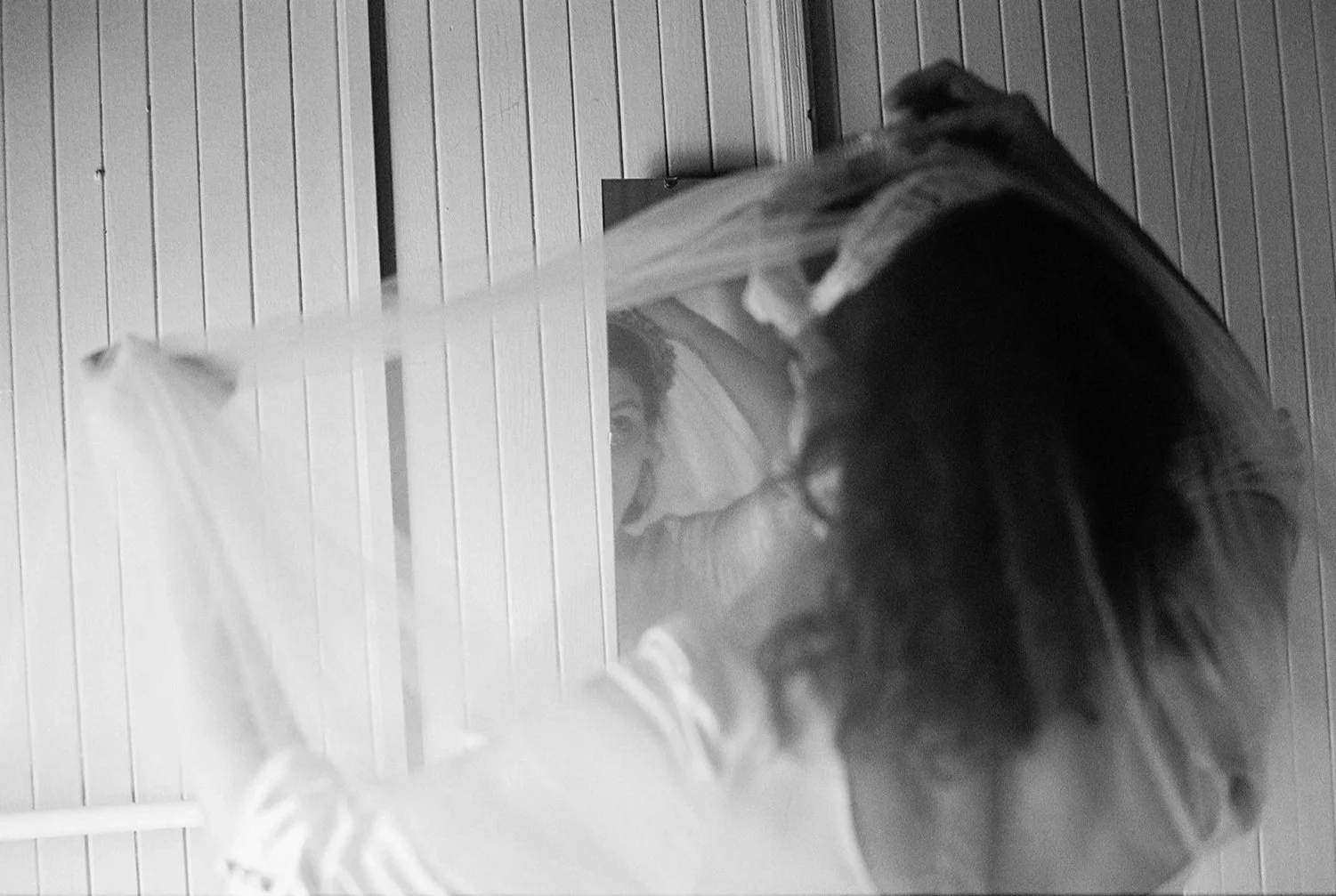 A woman with long dark hair taking a selfie in a mirror inside a room with wood paneling on the walls. She is wearing a hoodie.