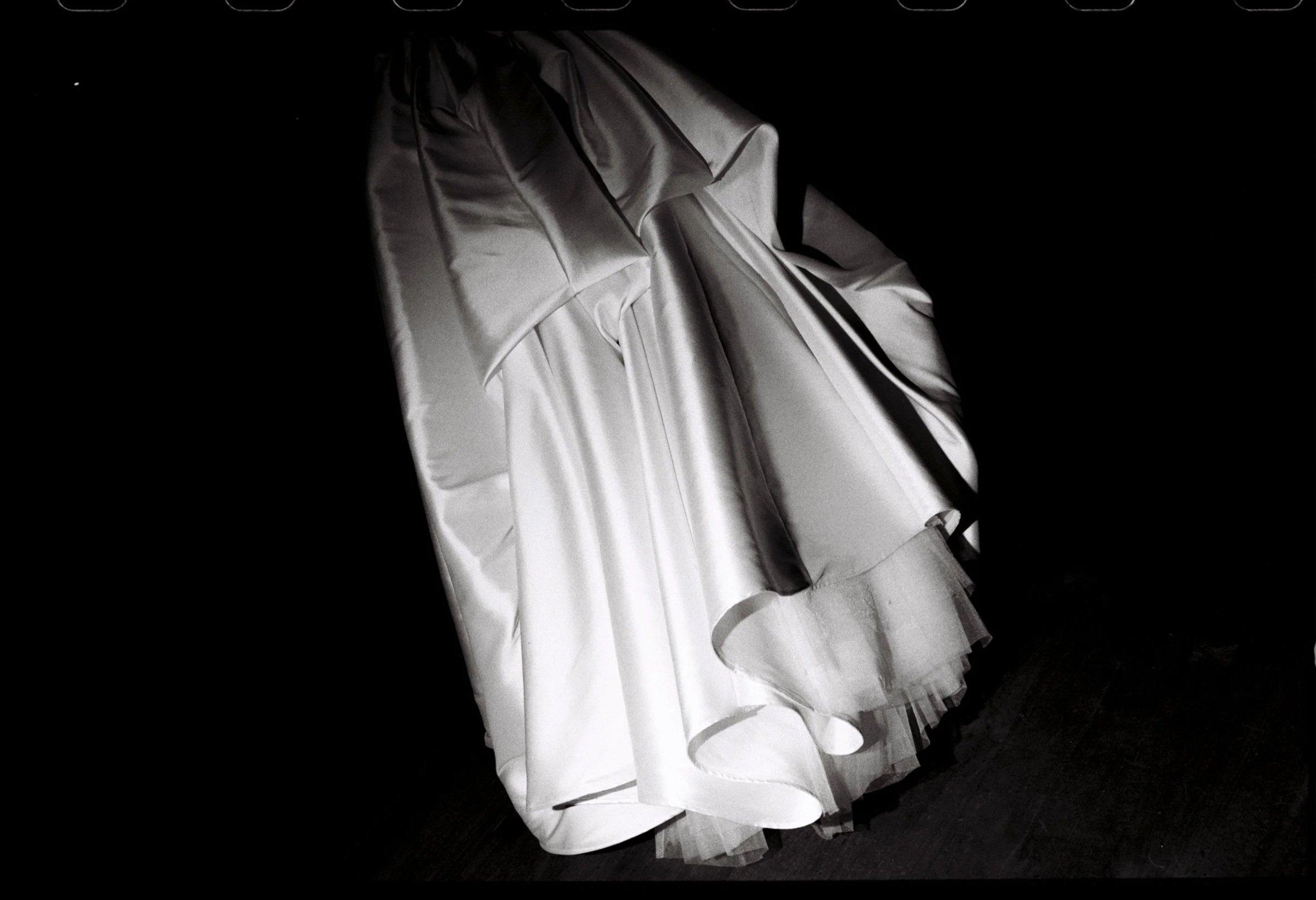 A wedding dress with a strapless bodice and full skirt, draped on a hanger against a dark background.