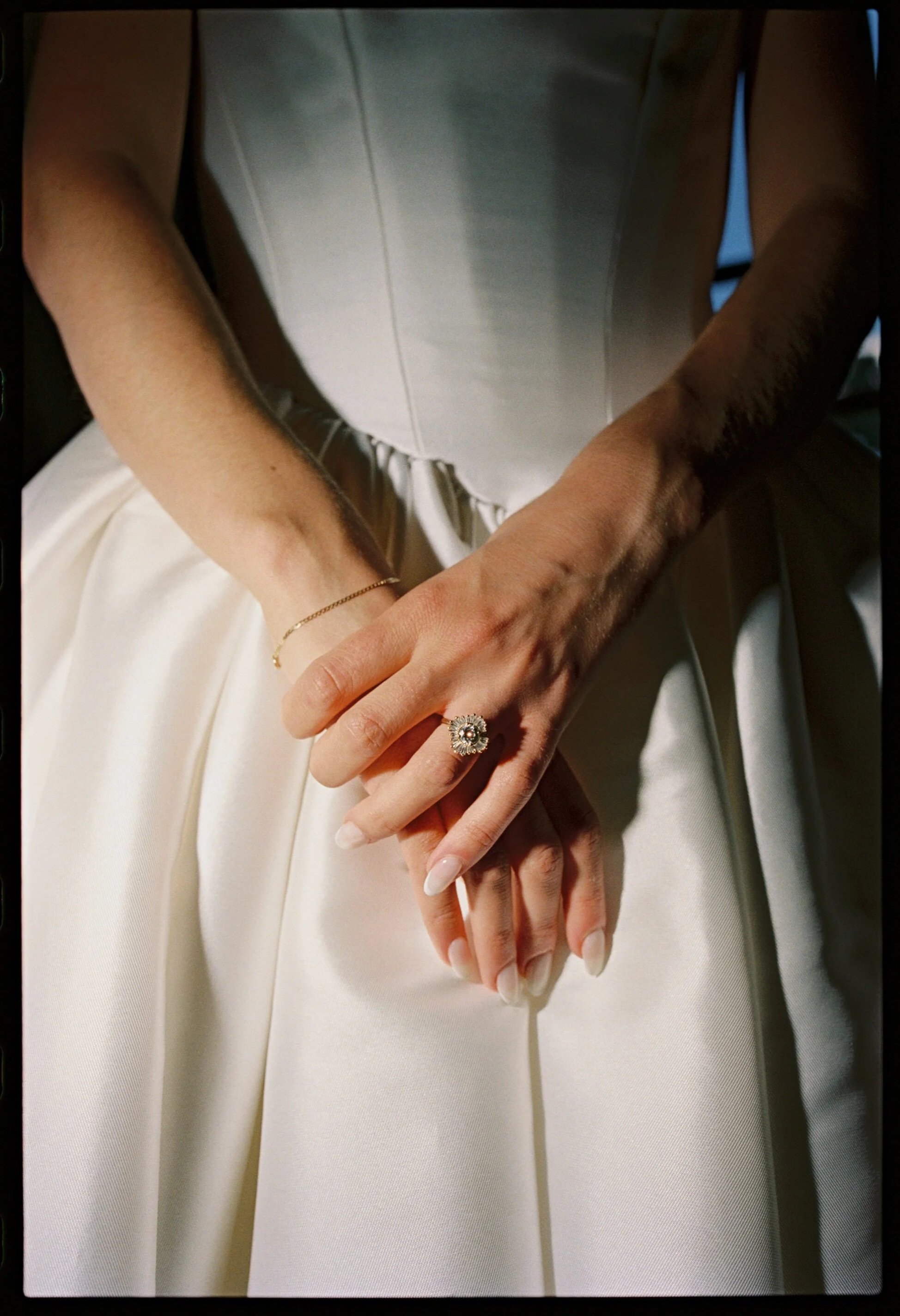 Close-up of a woman's hands with a wedding ring, resting on her lap in a wedding dress. Non -traditional film wedding photographer in Maine. 