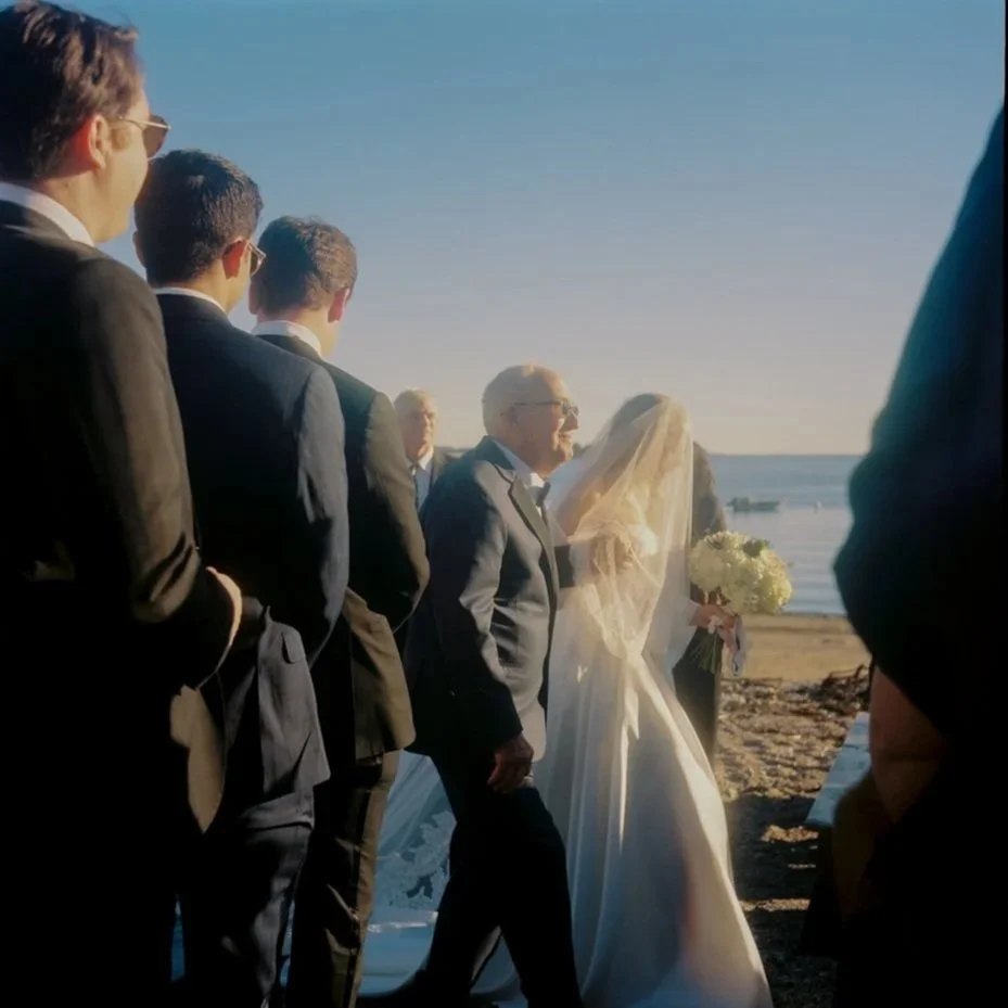 Wedding ceremony on the beach with a bride, groom, and groomsmen in suits, with ocean in the background.Non -traditional film wedding photographer in Maine. 
