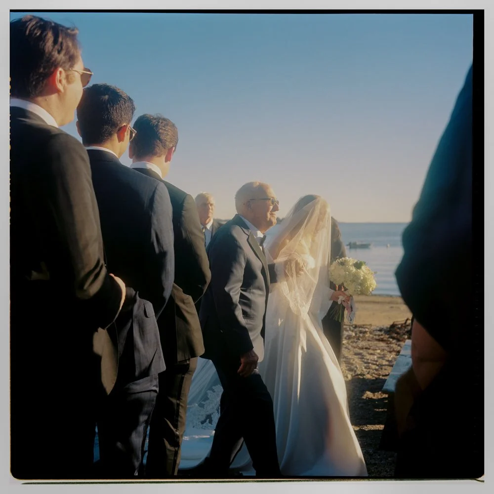Wedding ceremony on the beach with a bride, groom, and groomsmen in suits, with ocean in the background.Non -traditional film wedding photographer in Maine. 