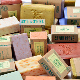 A collection of various handmade soap bars wrapped in paper and cardboard packaging, displayed together.