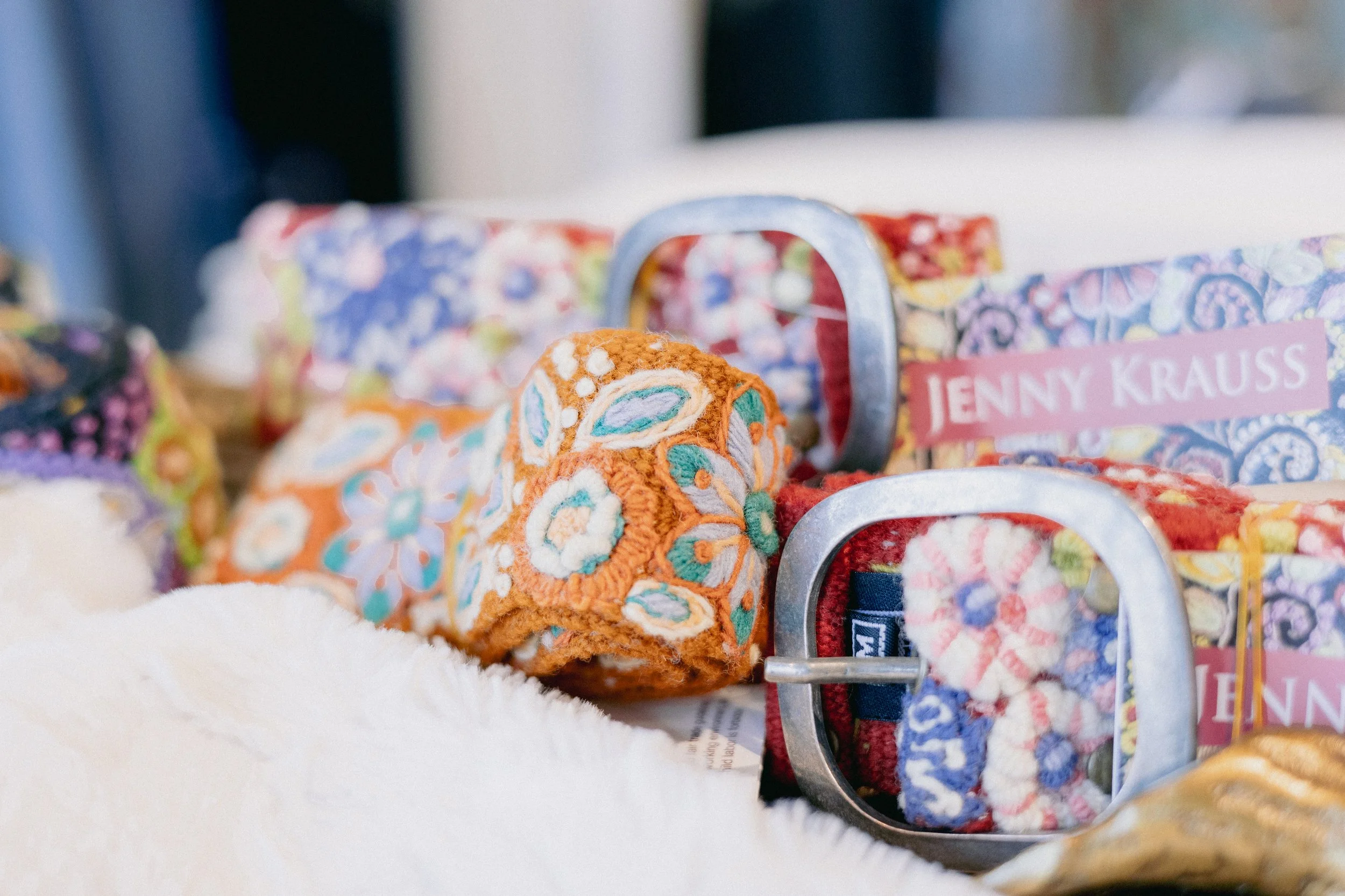 Assorted colorful fabric rolls with embroidery and tags, displayed on a white surface.