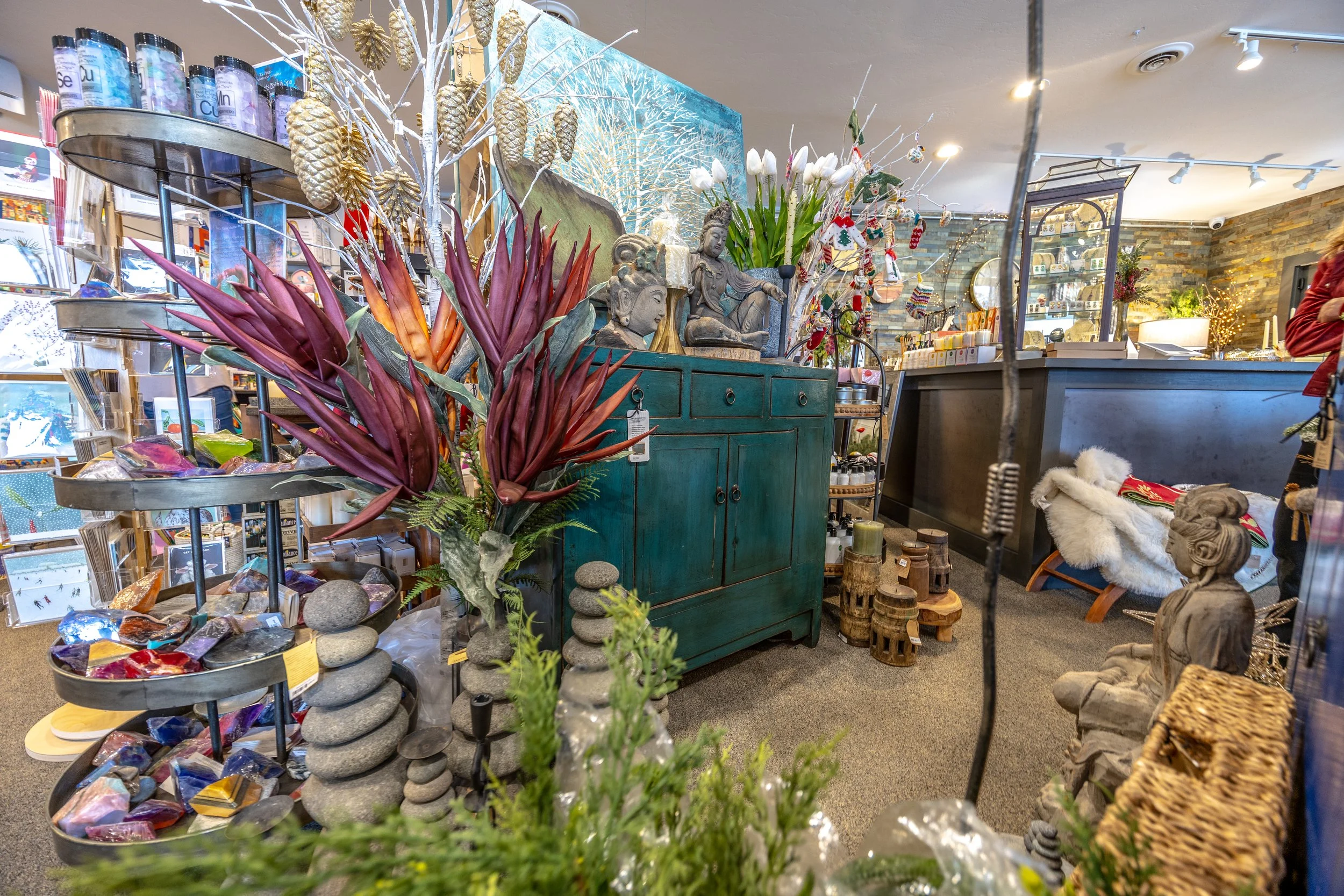 Interior of a retail store decorated for Christmas with various plants, statues, and decorative items on shelves and tables.