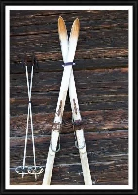 A pair of wooden snowshoes and two ski poles resting on a dark wooden surface.