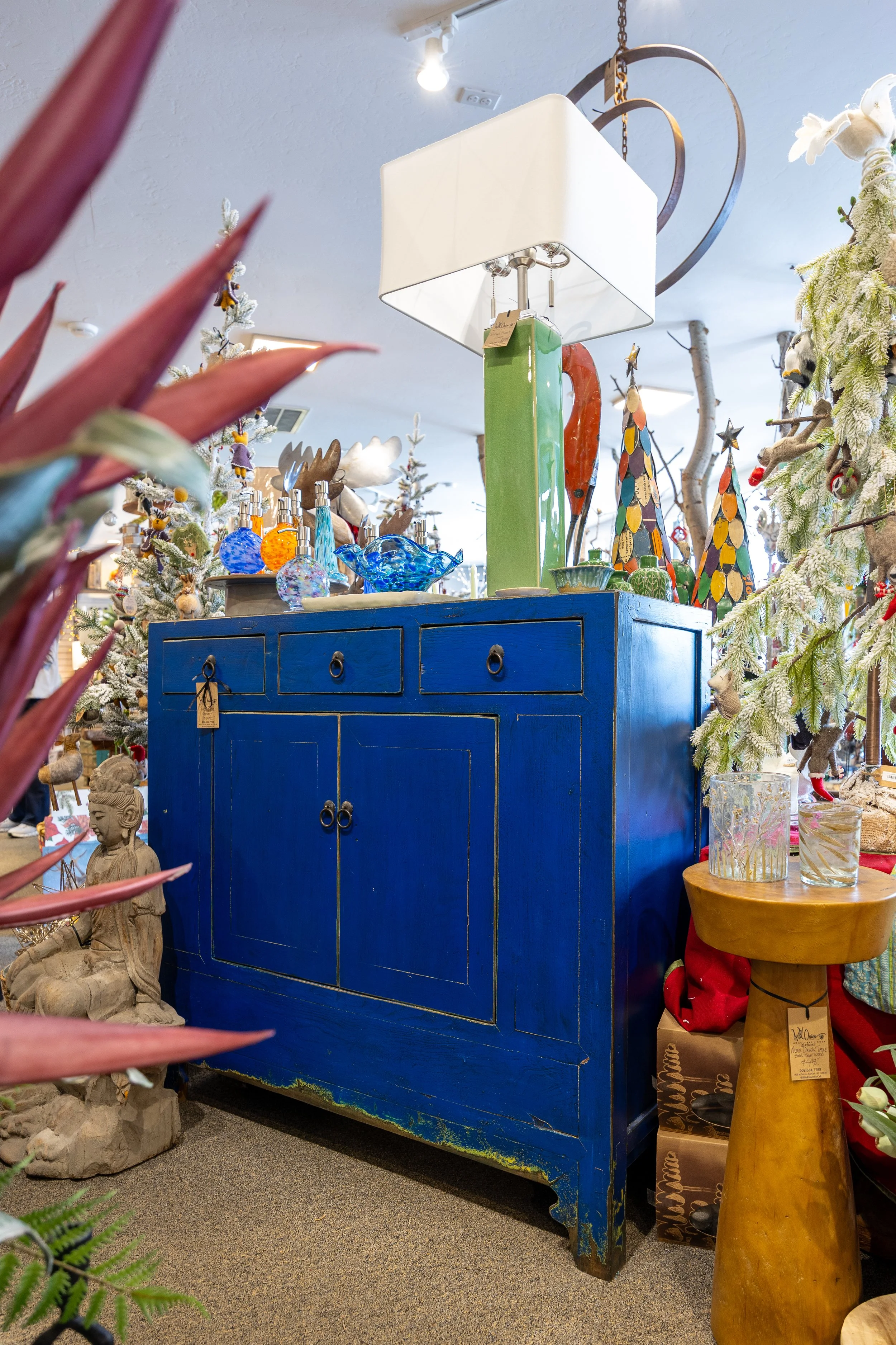 A display of various decorative items, including colorful glass bottles, sculptures, and wooden figures, arranged on a blue cabinet and nearby table in a store.