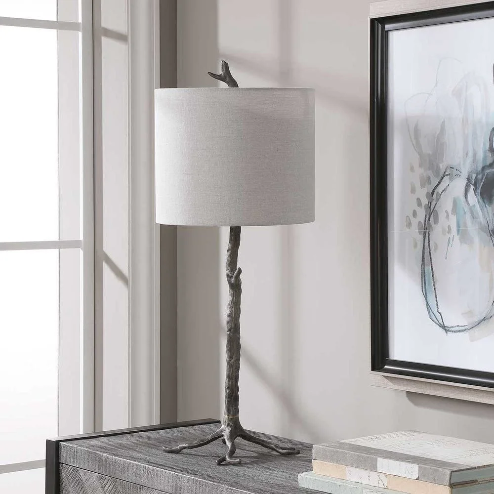 Table lamp made from a branch with a fiber drum shade on a wooden side table next to a framed artwork.''
