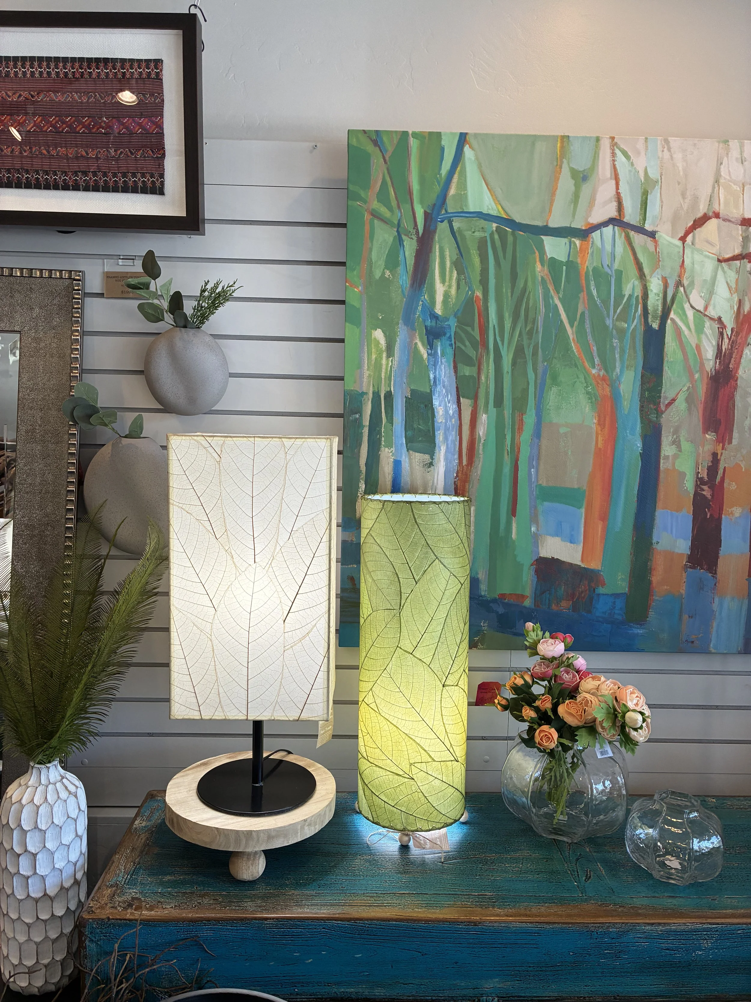 Decorative home display with framed artwork, vases, a lamp, and a bouquet of pink and peach roses on a blue wooden table.