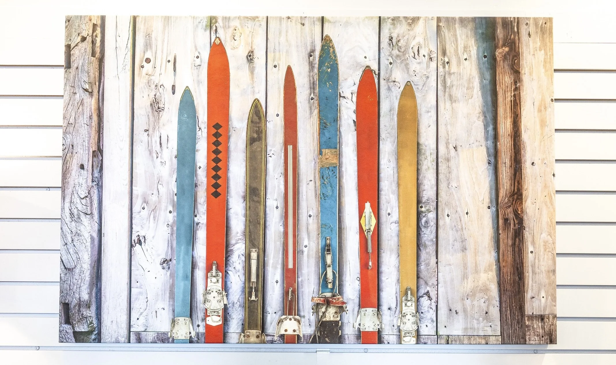 A display of vintage and modern skis mounted on a wooden wall with a slatwall in the background.