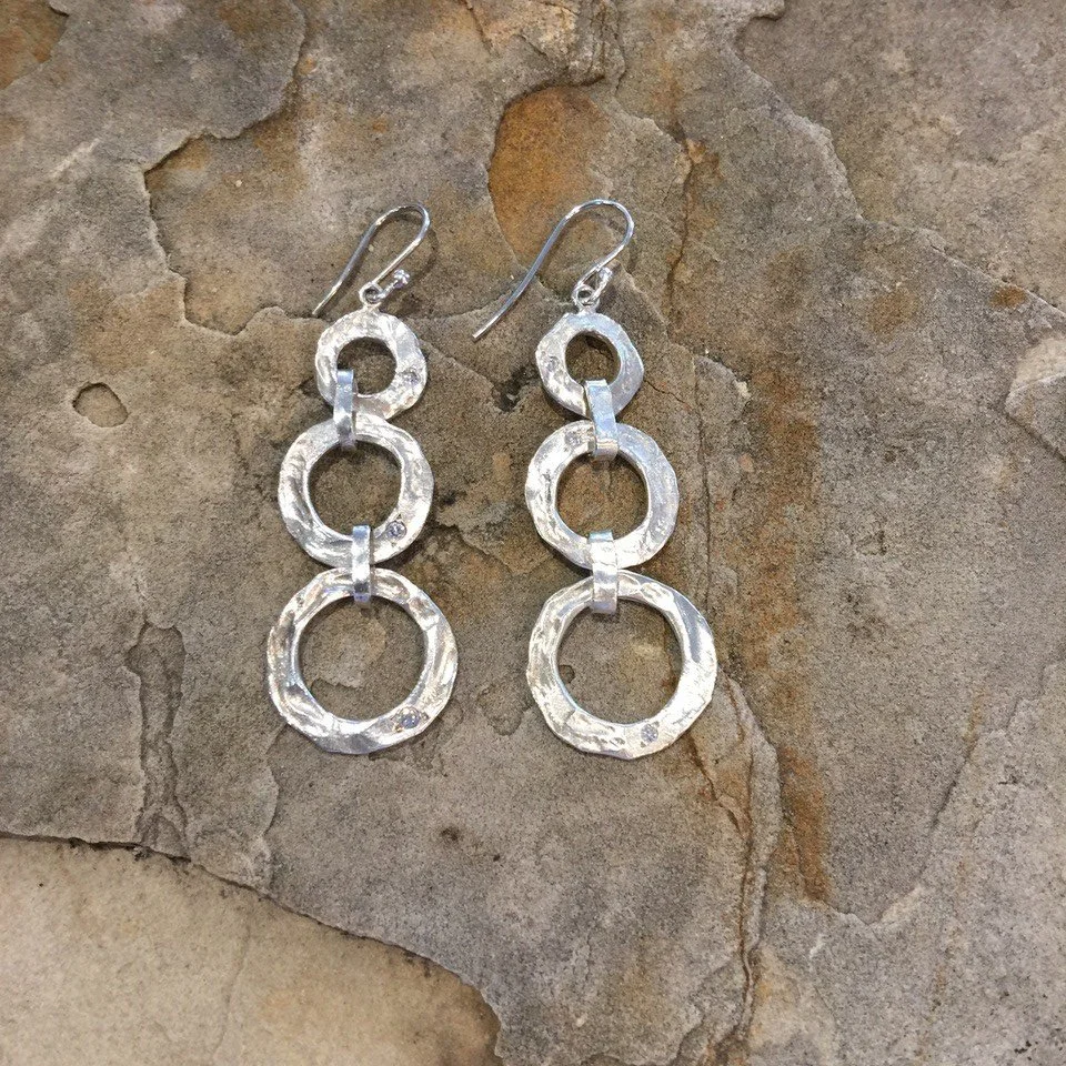 Pair of silver, textured circle earrings with hook fastenings on a stone background.
