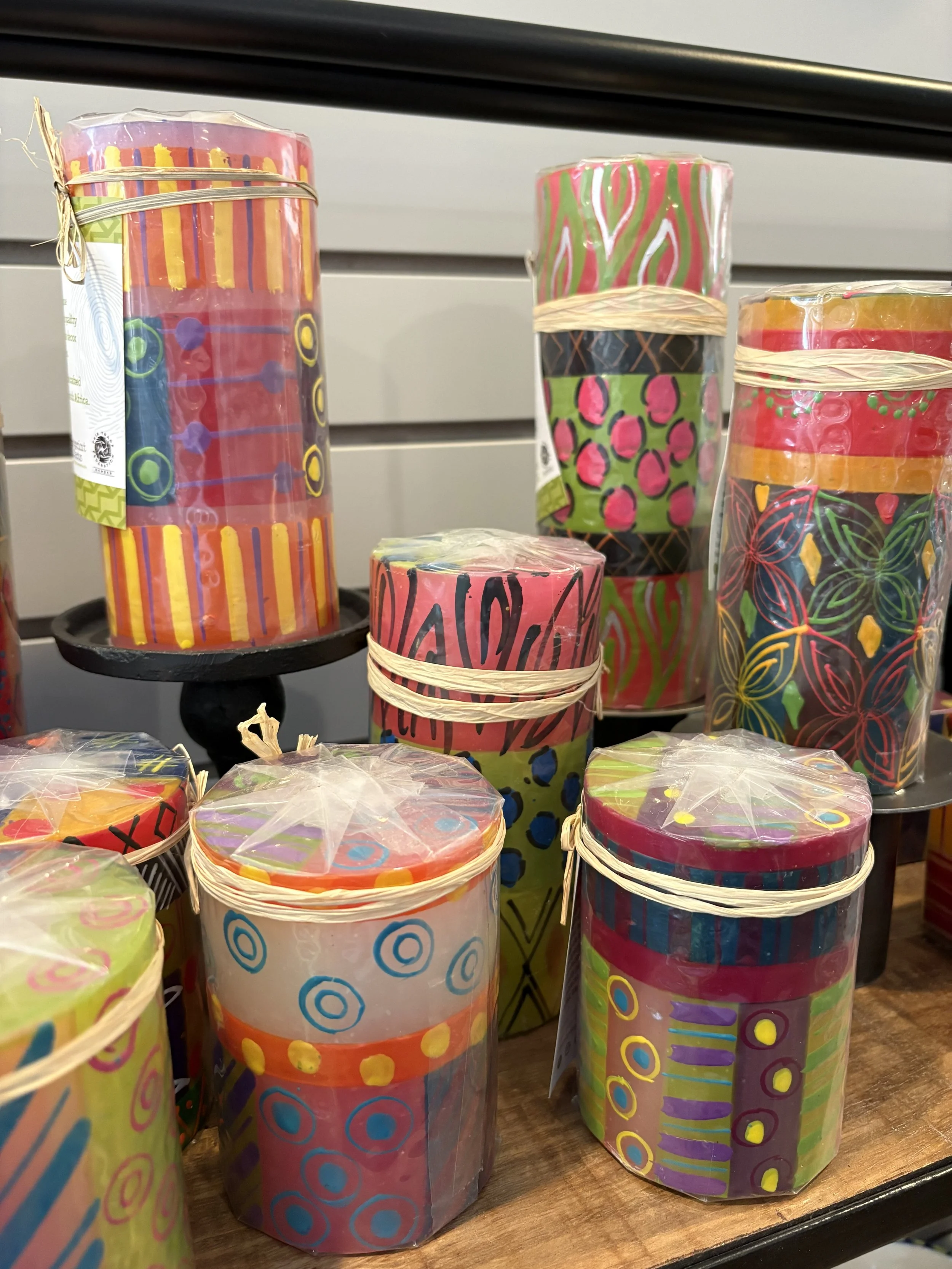 Colorful cylindrical fireworks with various patterns, wrapped in clear plastic, displayed on a wooden shelf.