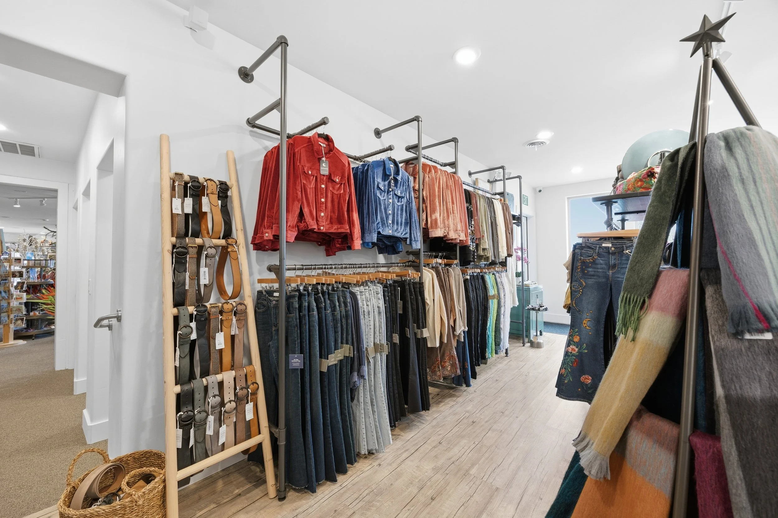 Interior of a clothing store with racks of colorful jackets, jeans, and accessories displayed on wooden shelves and metal racks.