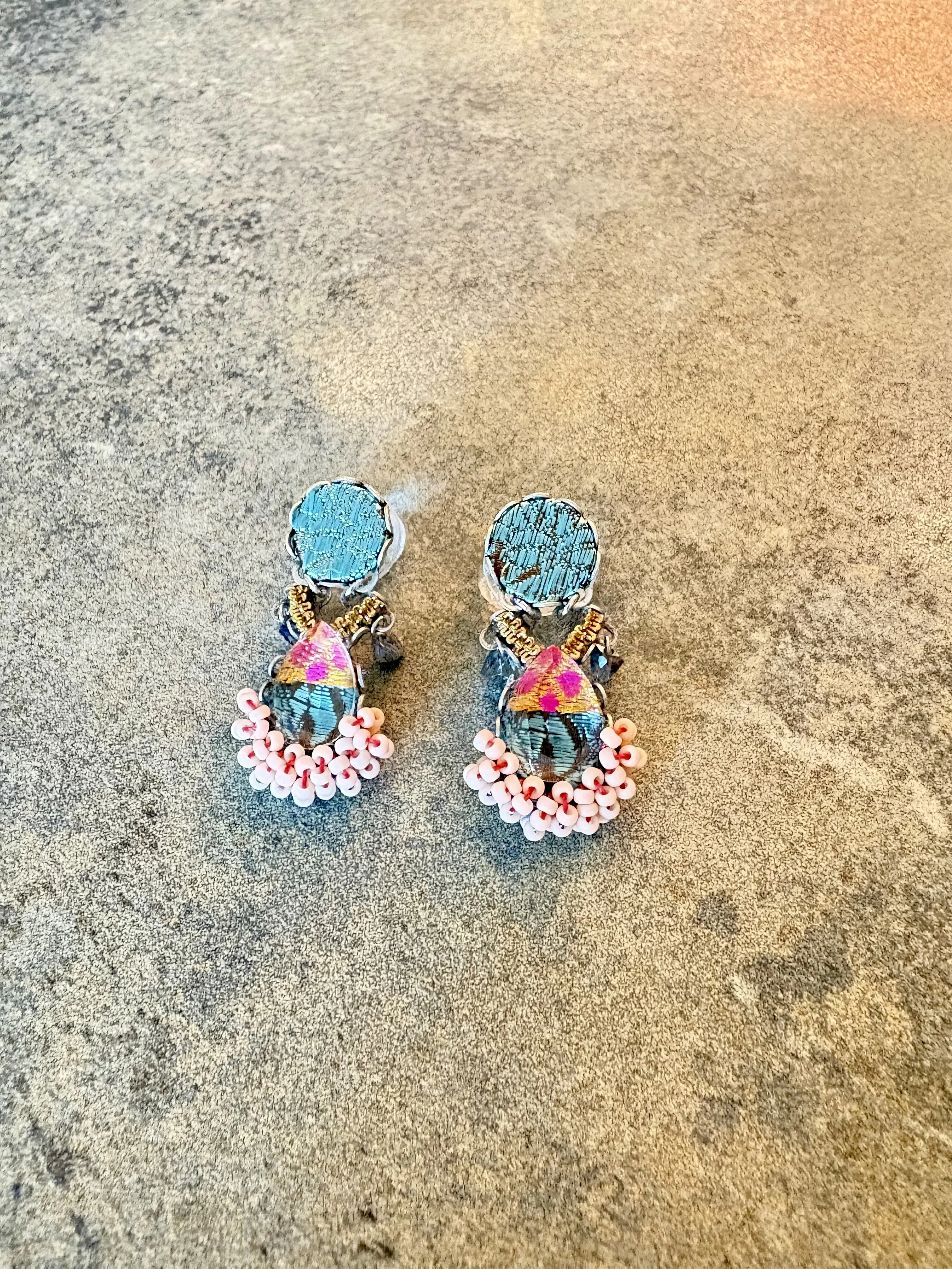 Pair of colorful earrings with blue, pink, and gold beads on a gray textured surface.