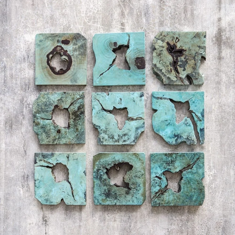 Nine square turquoise and green distressed metal sheets with rusted holes arranged in a three-by-three grid on a concrete wall.