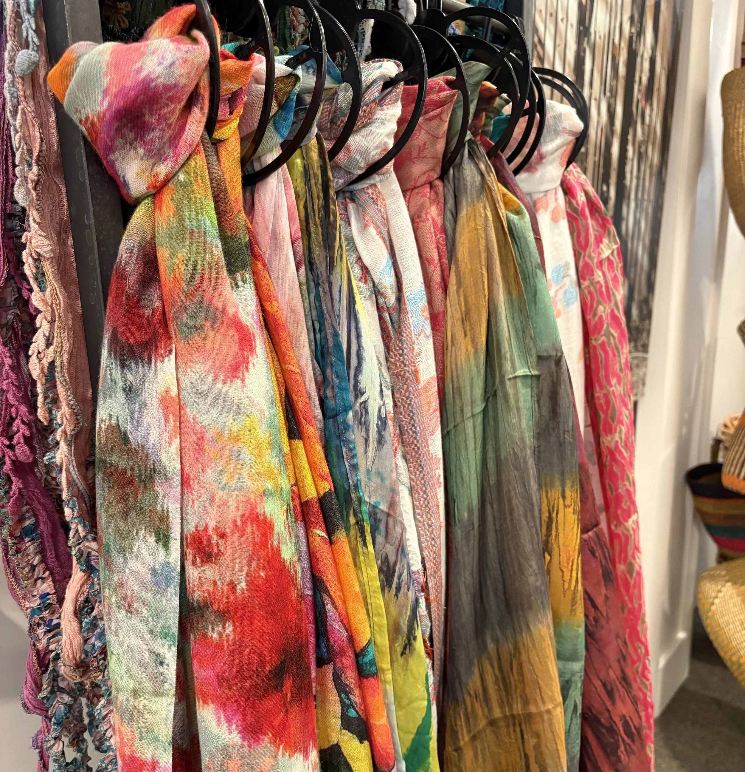 A row of colorful, patterned scarves hanging on black hooks in a store or boutique.