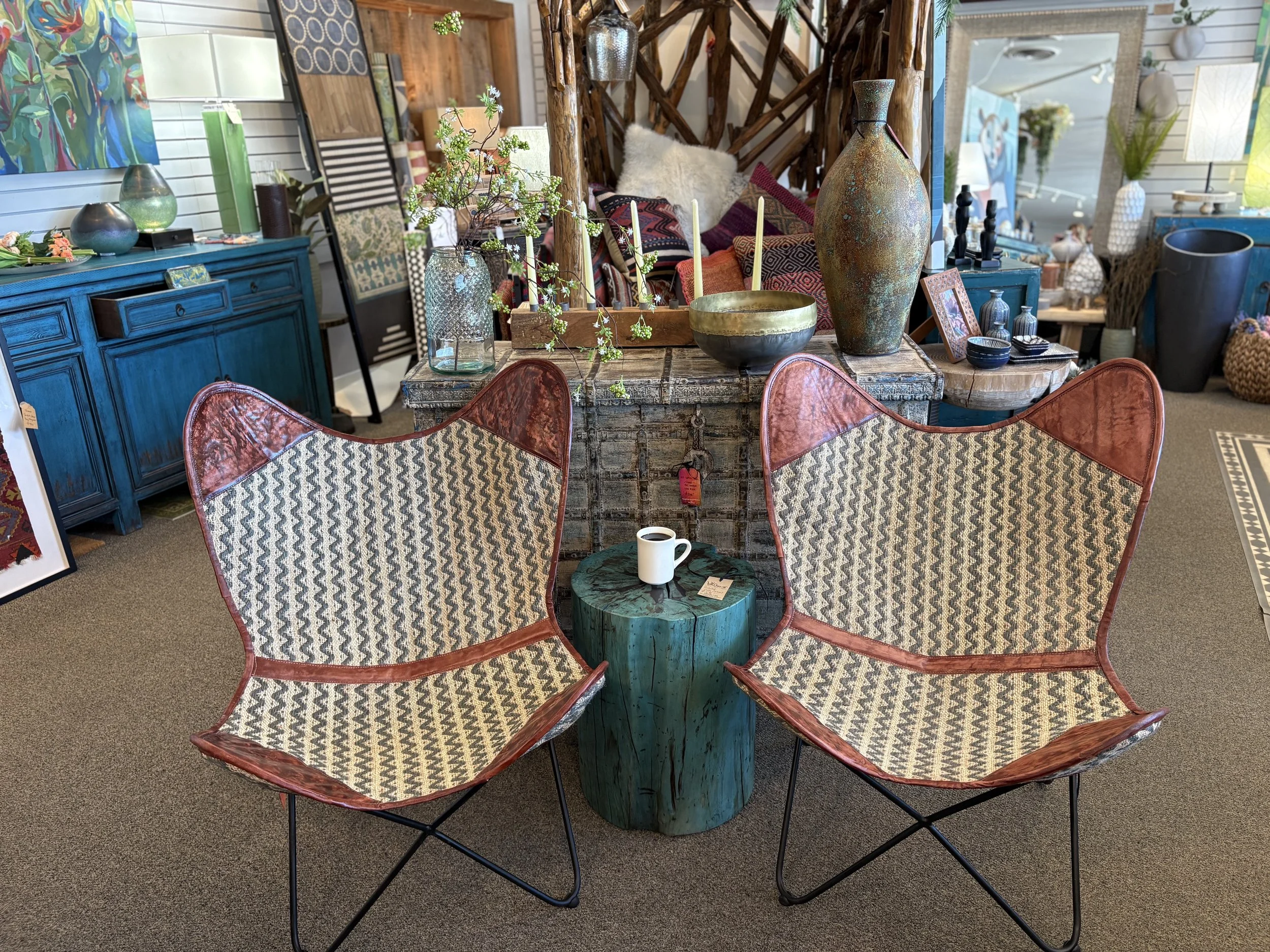 Decorative rustic furniture and home decor items in a store, including a blue sideboard, vases, candles, artwork, and chairs with patterned cushions.