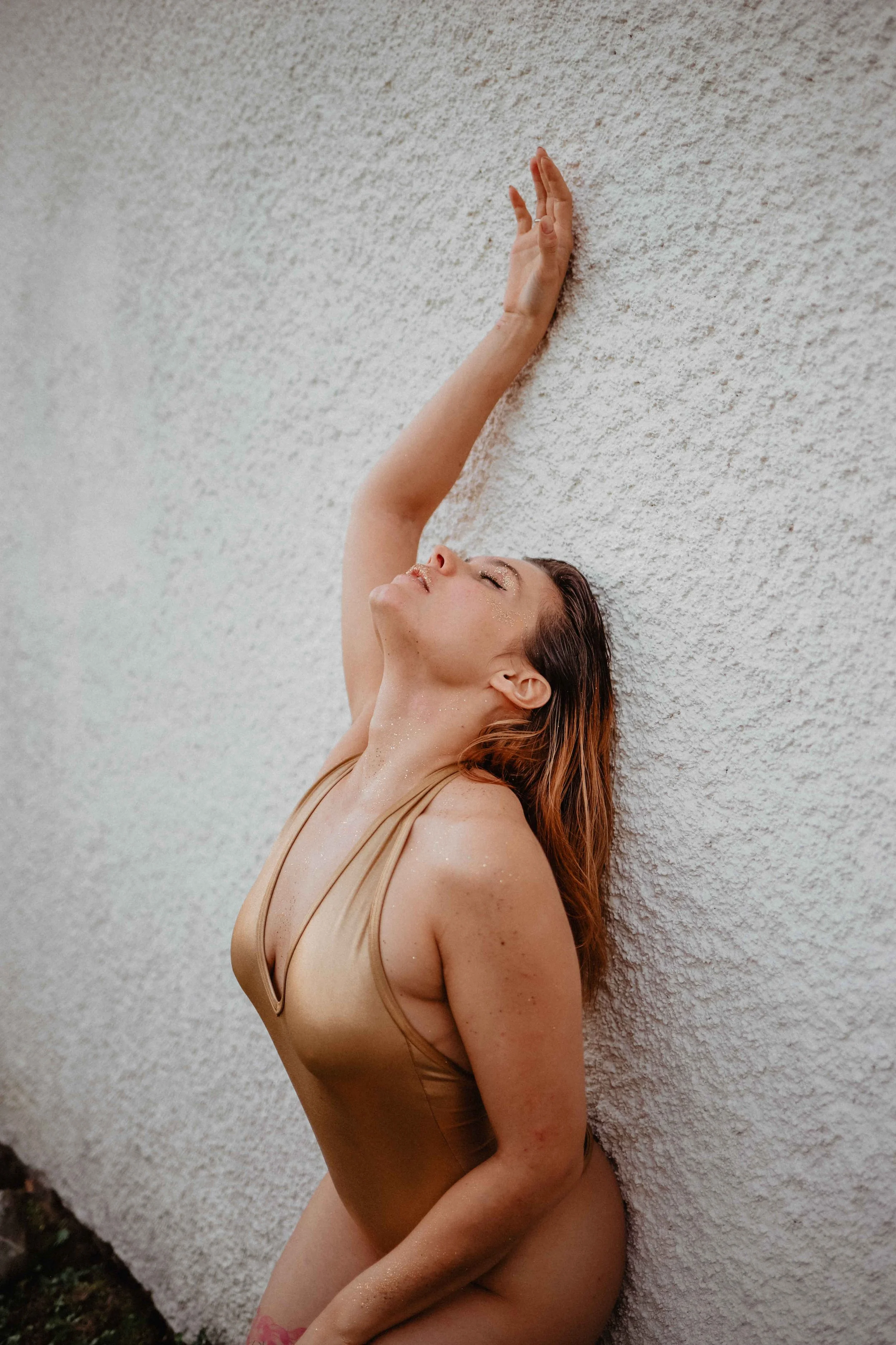 Une femme en maillot beige pose contre un mur blanc avec une expression de détente.