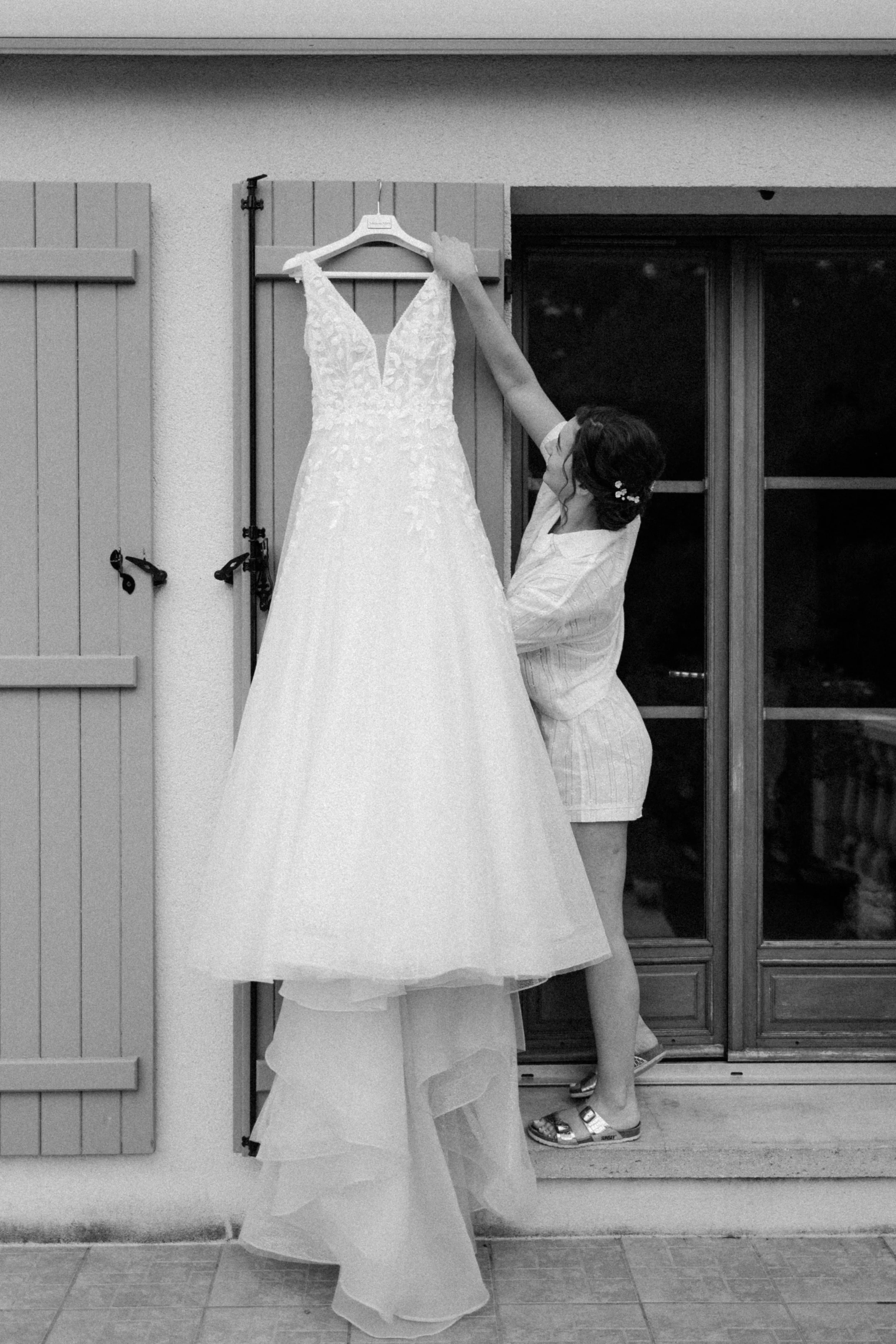 Femme regardant une robe de mariage blanche suspendue à une porte-fenêtre.