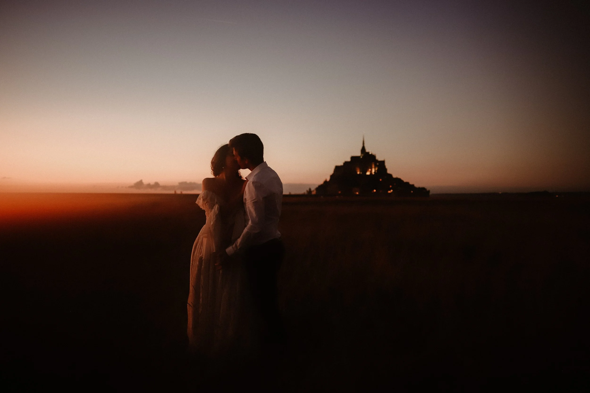 Un couple en silhouette s'embrassant au coucher du soleil devant un temple sur une île.