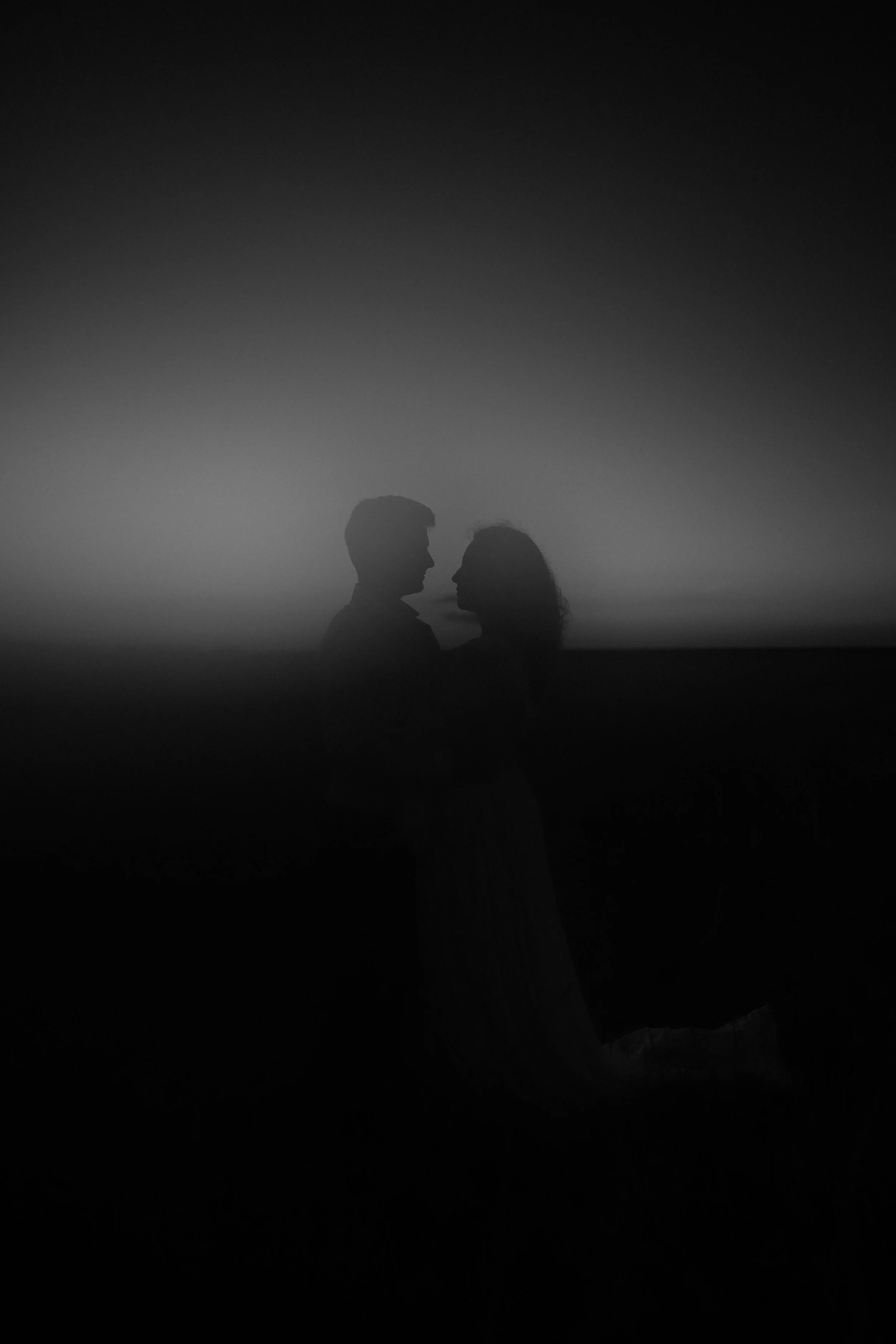 Silhouettes d'un homme et d'une femme qui se regardent tendrement au coucher du soleil, en noir et blanc.